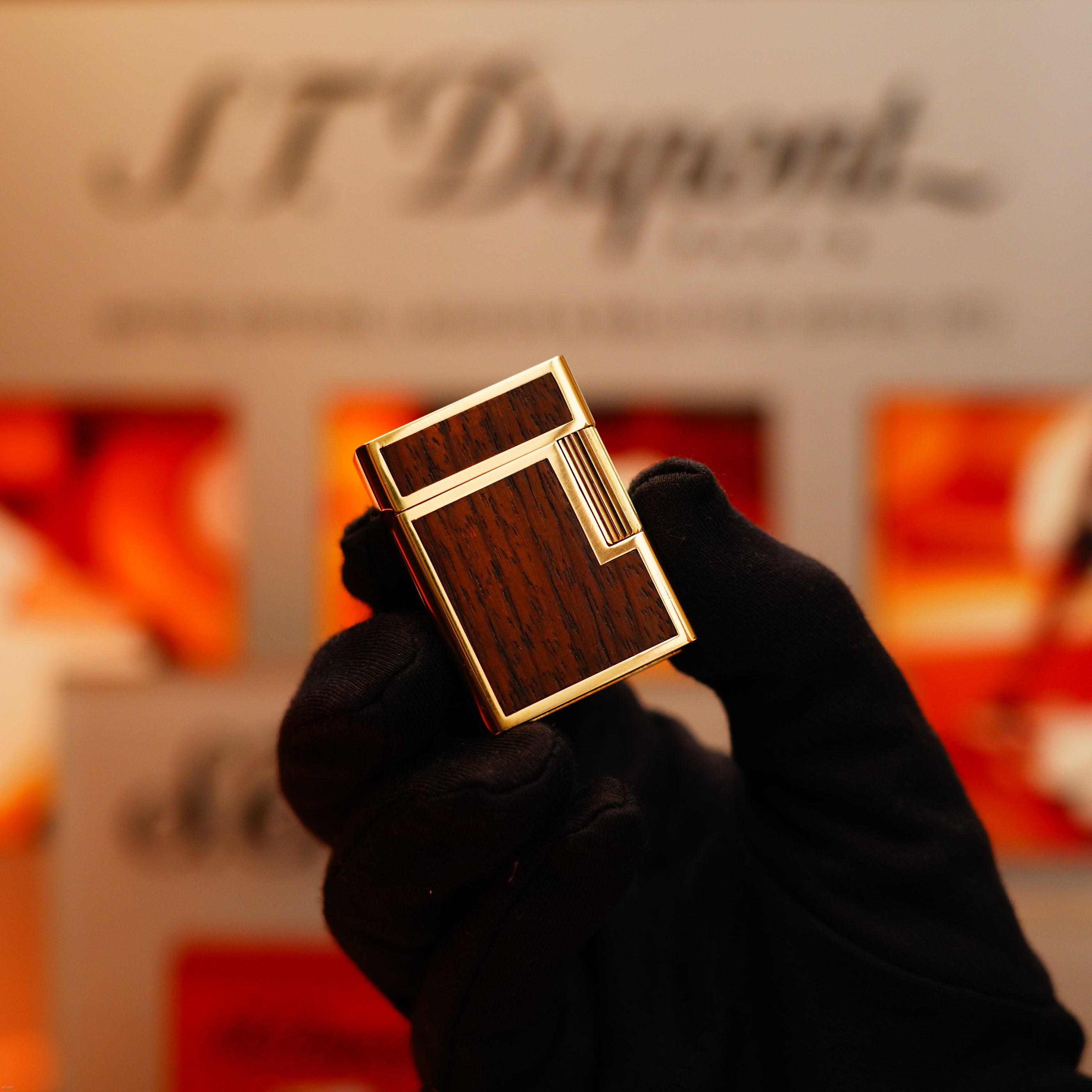 A gloved hand holds a Vintage 1970 Rare S.T. Dupont Solid 18k Gold and Natural Wood 750 hallmarked lighter, set against a blurred branded background.