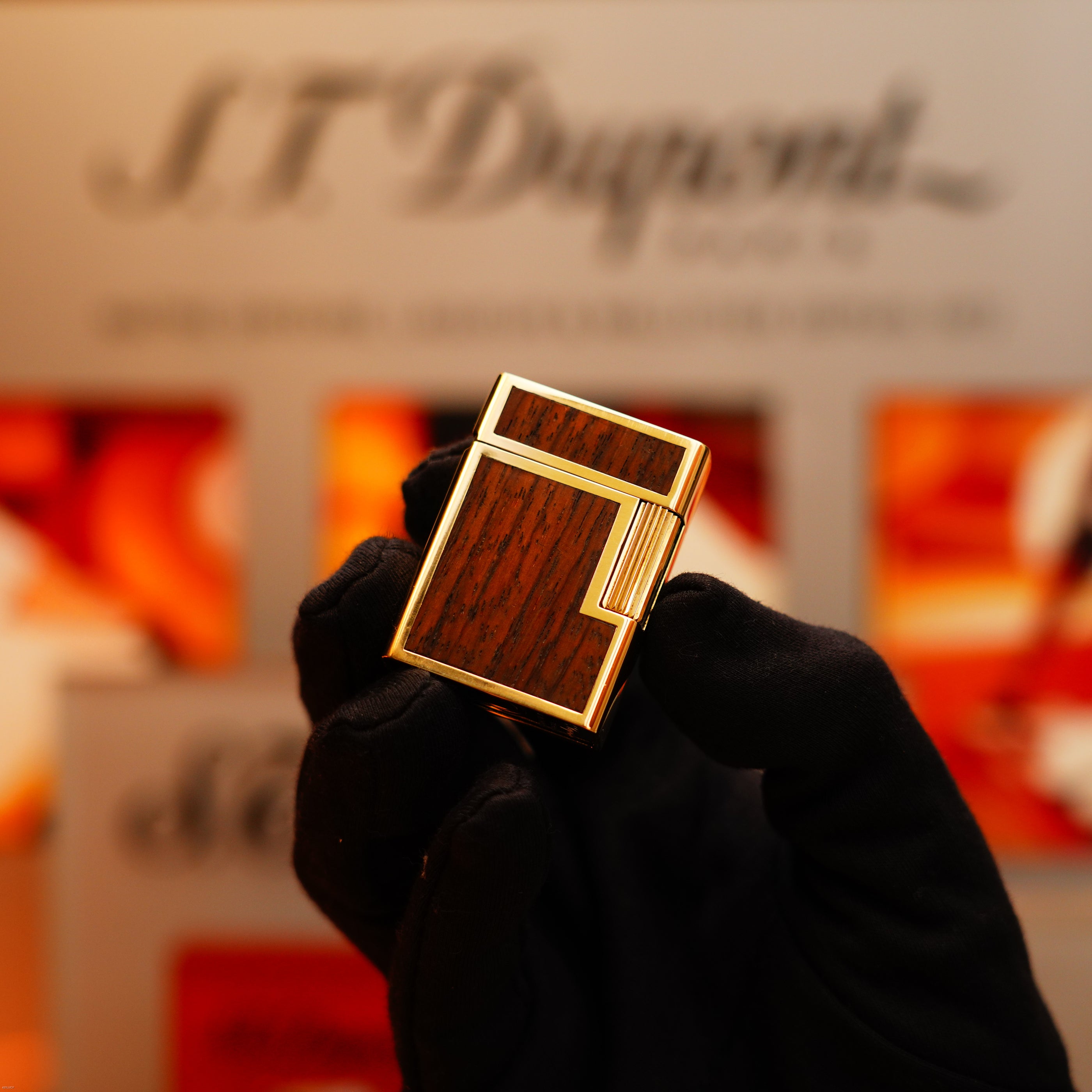 A gloved hand displays a Vintage 1970 Rare S.T. Dupont Solid 18k Gold and Natural Wood 750 hallmarked lighter, with the brand's logo blurred in the background.
