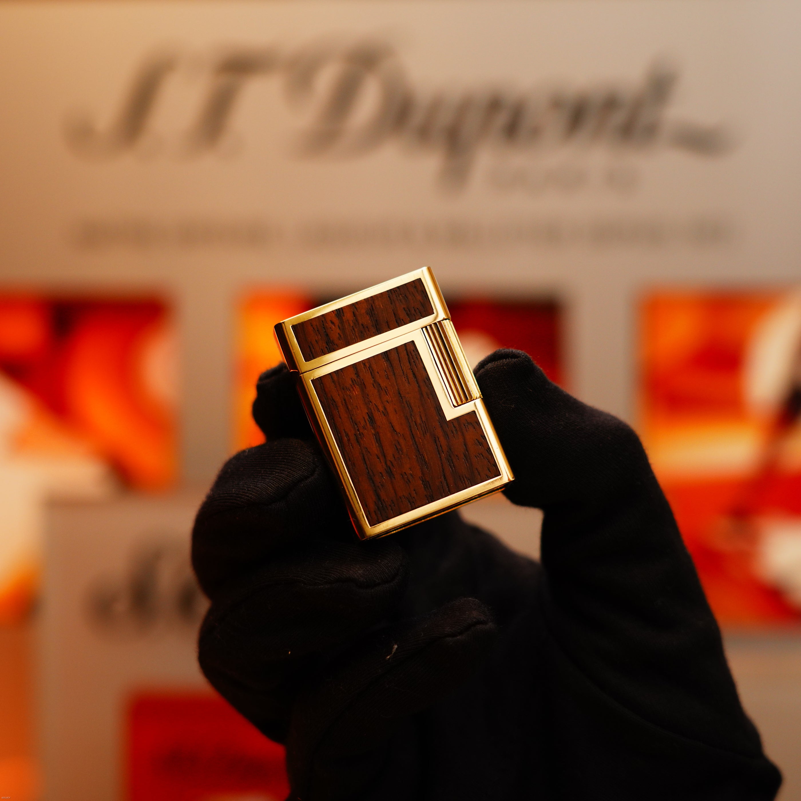 A hand in a black glove holds a Vintage 1970 Rare S.T. Dupont Solid 18k Gold and Natural Wood 750 hallmarked Lighter against a blurred background with the S.T. Dupont logo.