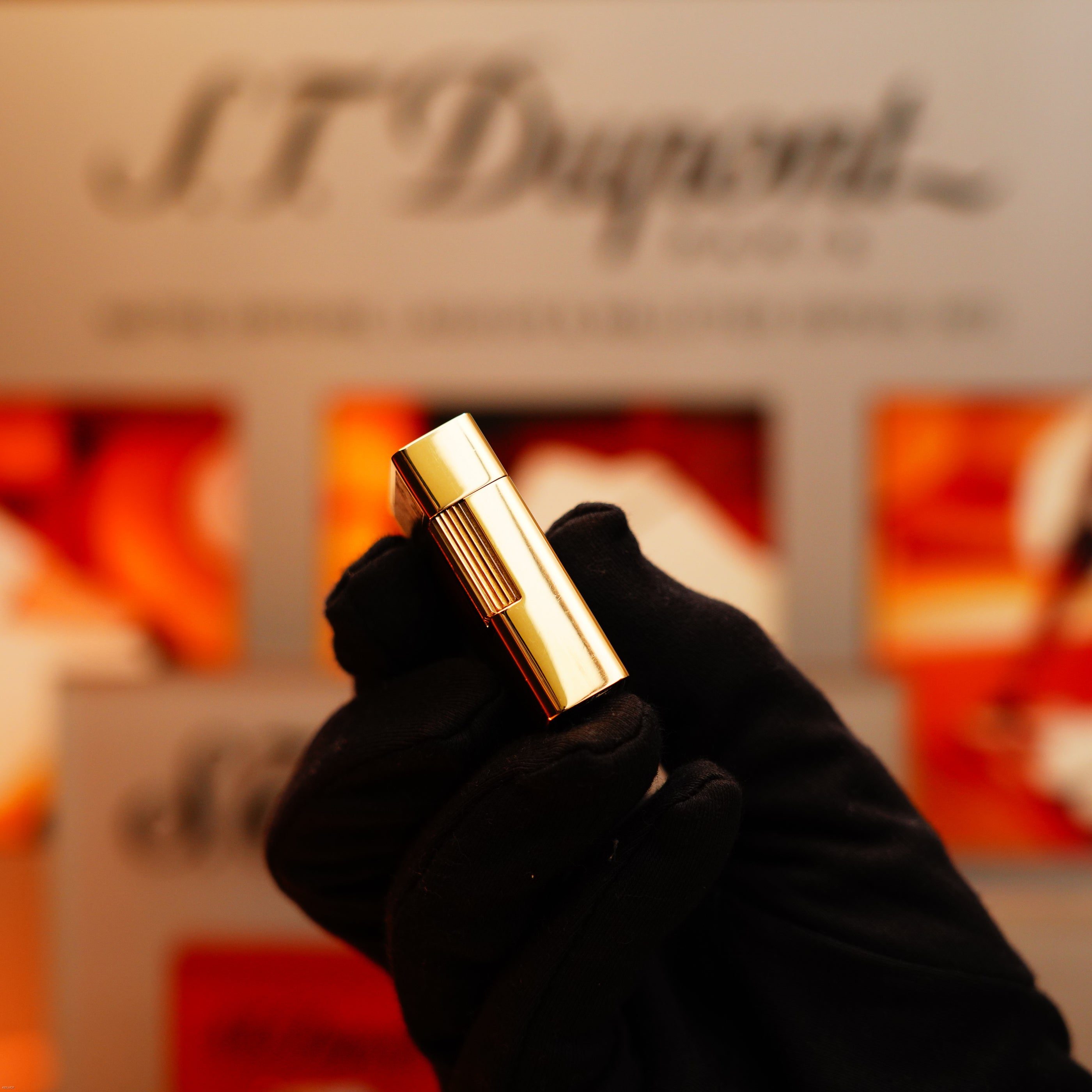 A gloved hand holds a Vintage 1970 Rare S.T. Dupont Solid 18k Gold and Natural Wood Lighter (750 hallmarked) against a blurred background with the S.T. Dupont logo and red accents.