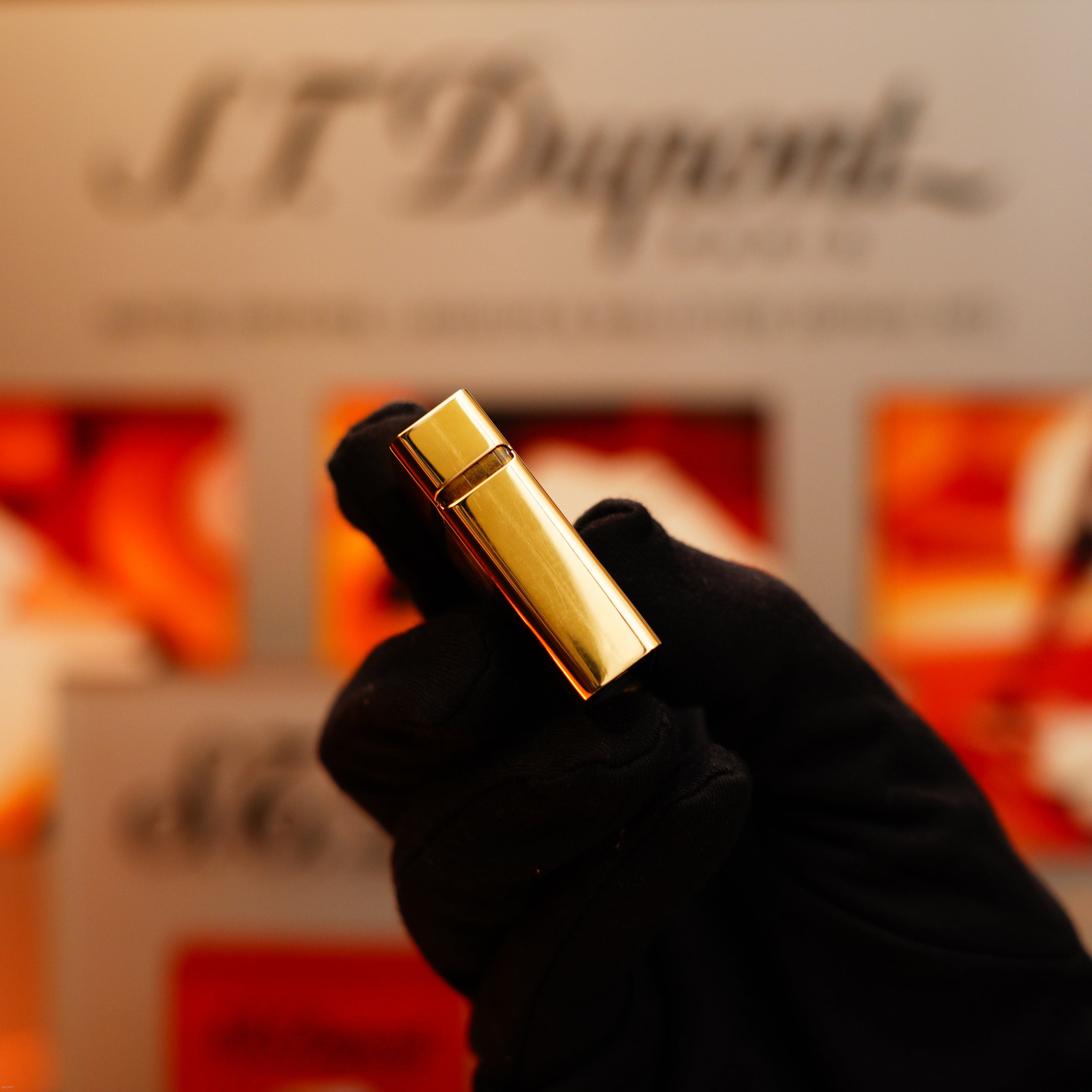 A gloved hand holds an S.T. Dupont Vintage 1970 Rare Solid 18k Gold and Natural Wood work 750 hallmarked Lighter, with the brand's blurred sign and a colorful background behind it.