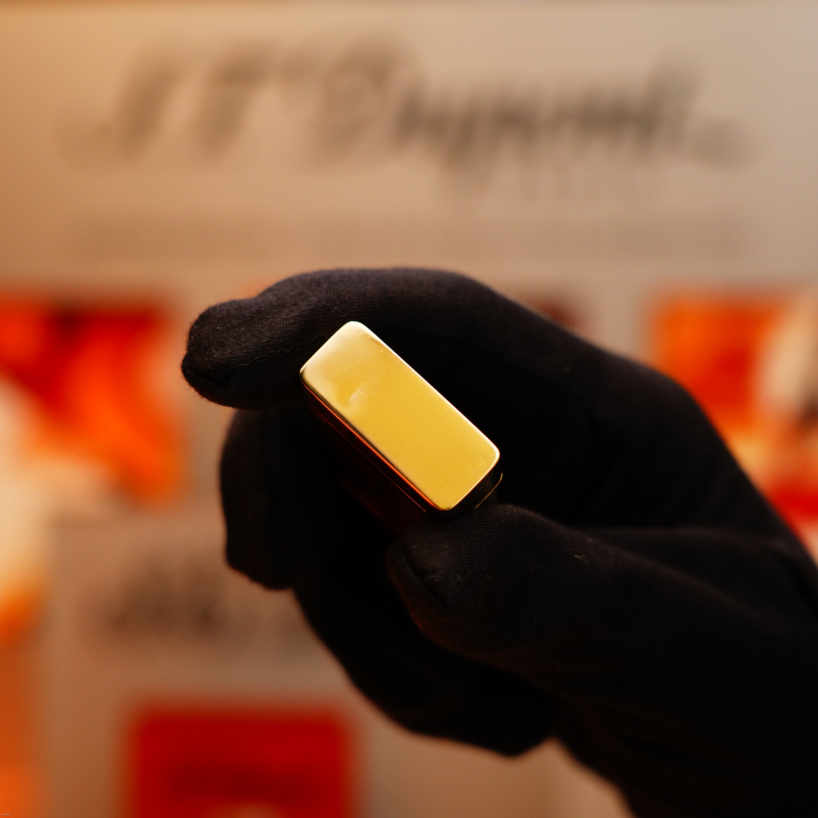 A gloved hand holds a Vintage 1970 Rare S.T. Dupont Solid 18k Gold and Natural Wood Work Lighter, hallmarked 750, with orange elements blurred in the background.