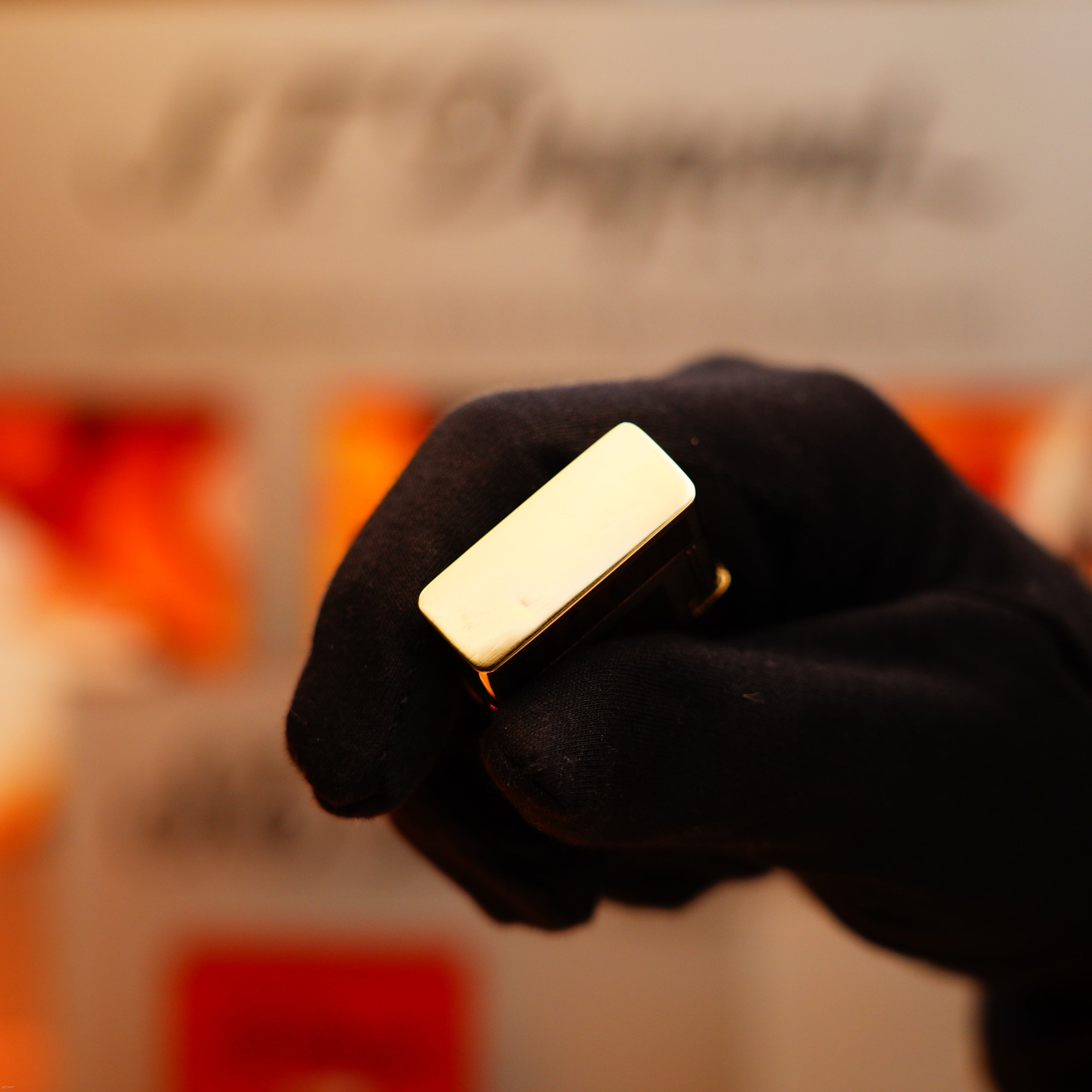 A gloved hand holds a Vintage 1970 Rare S.T. Dupont Solid 18k Gold and Natural Wood 750 hallmarked Lighter against a blurred background with indistinct text.