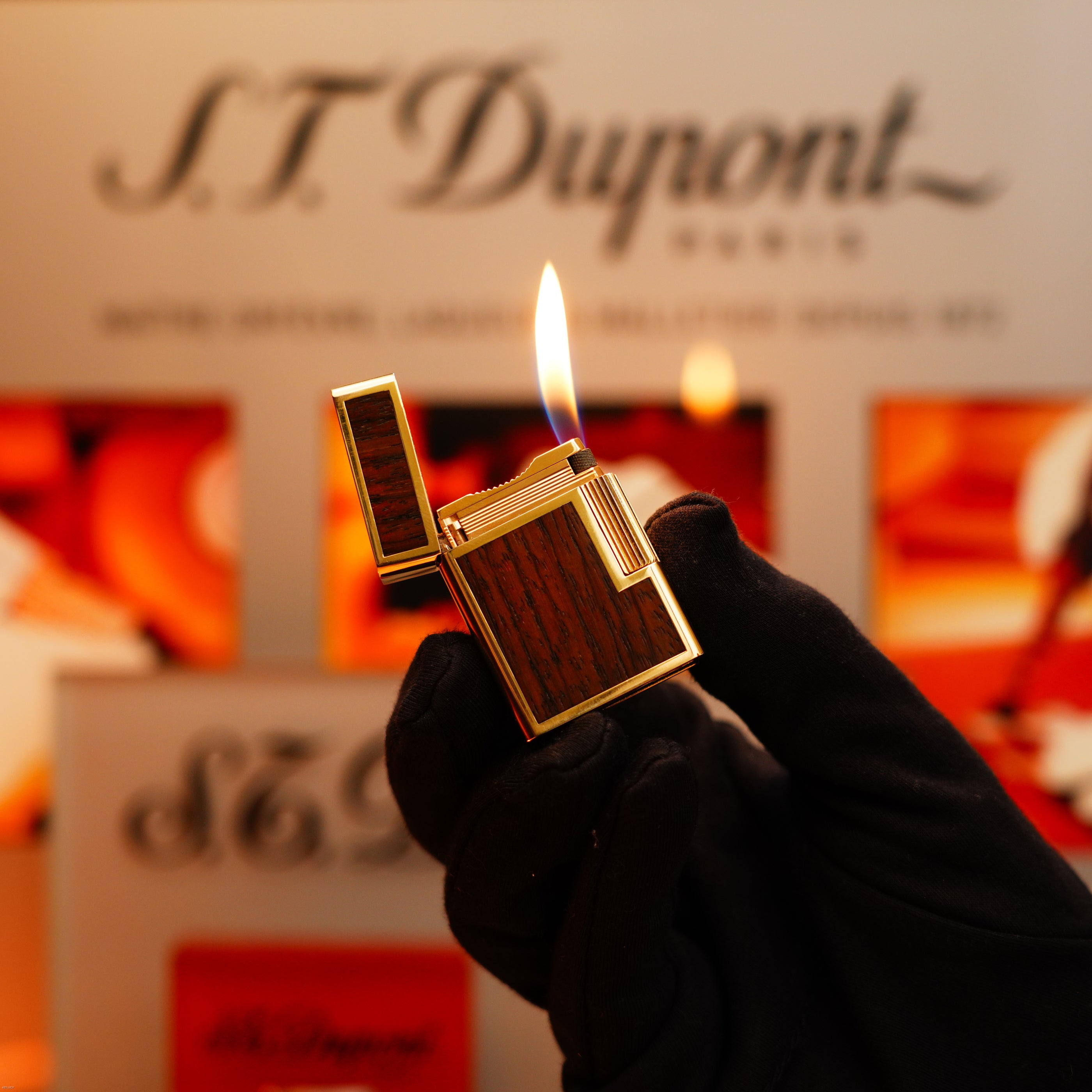 A gloved hand holds a Vintage 1970 Rare S.T. Dupont Solid 18k Gold and Natural Wood 750 hallmarked Lighter before a blurred S.T. Dupont display.