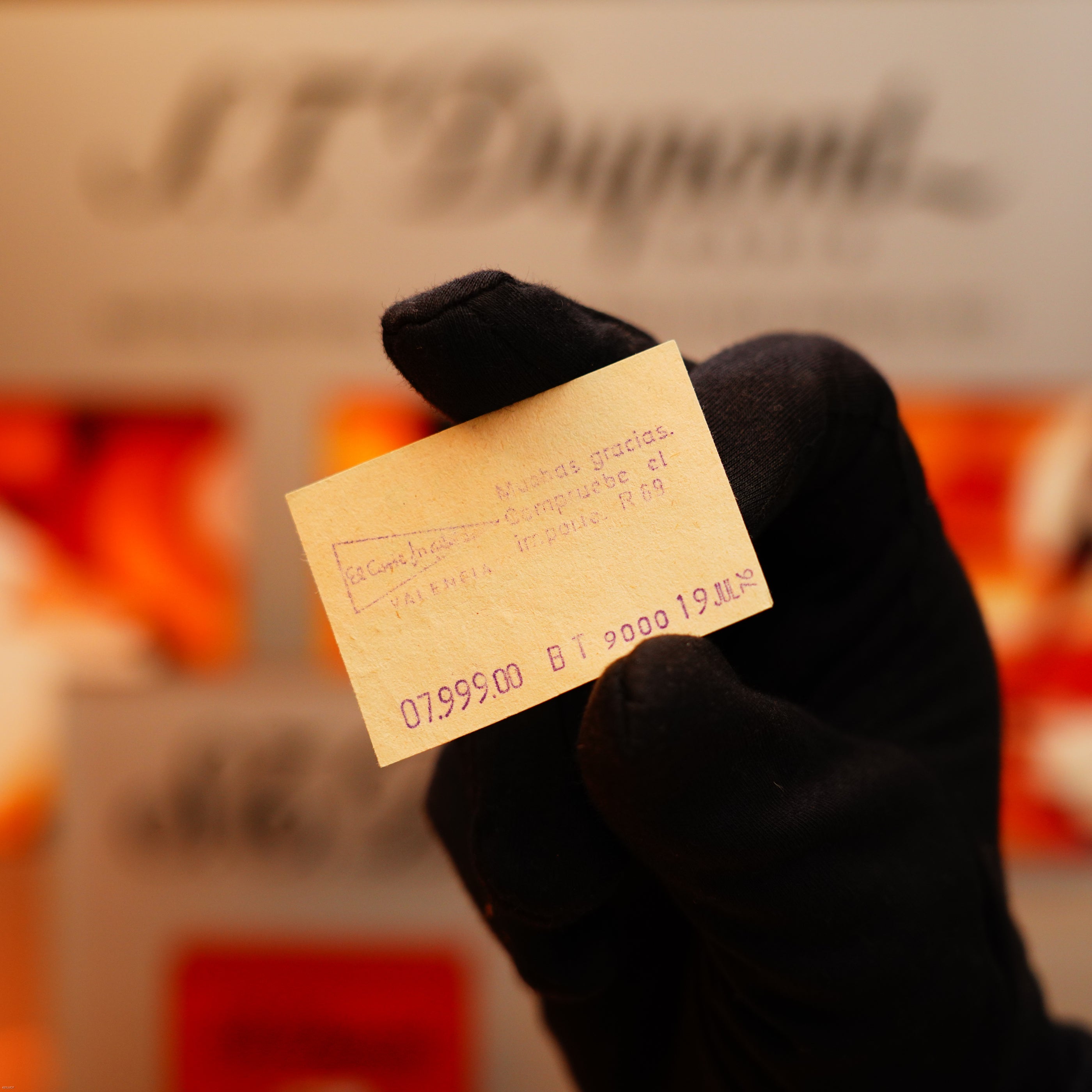 A gloved hand holds a Vintage 1970 Rare S.T. Dupont Solid 18k Gold and Natural Wood work 750 hallmarked lighter; blurred background with indistinct signage.