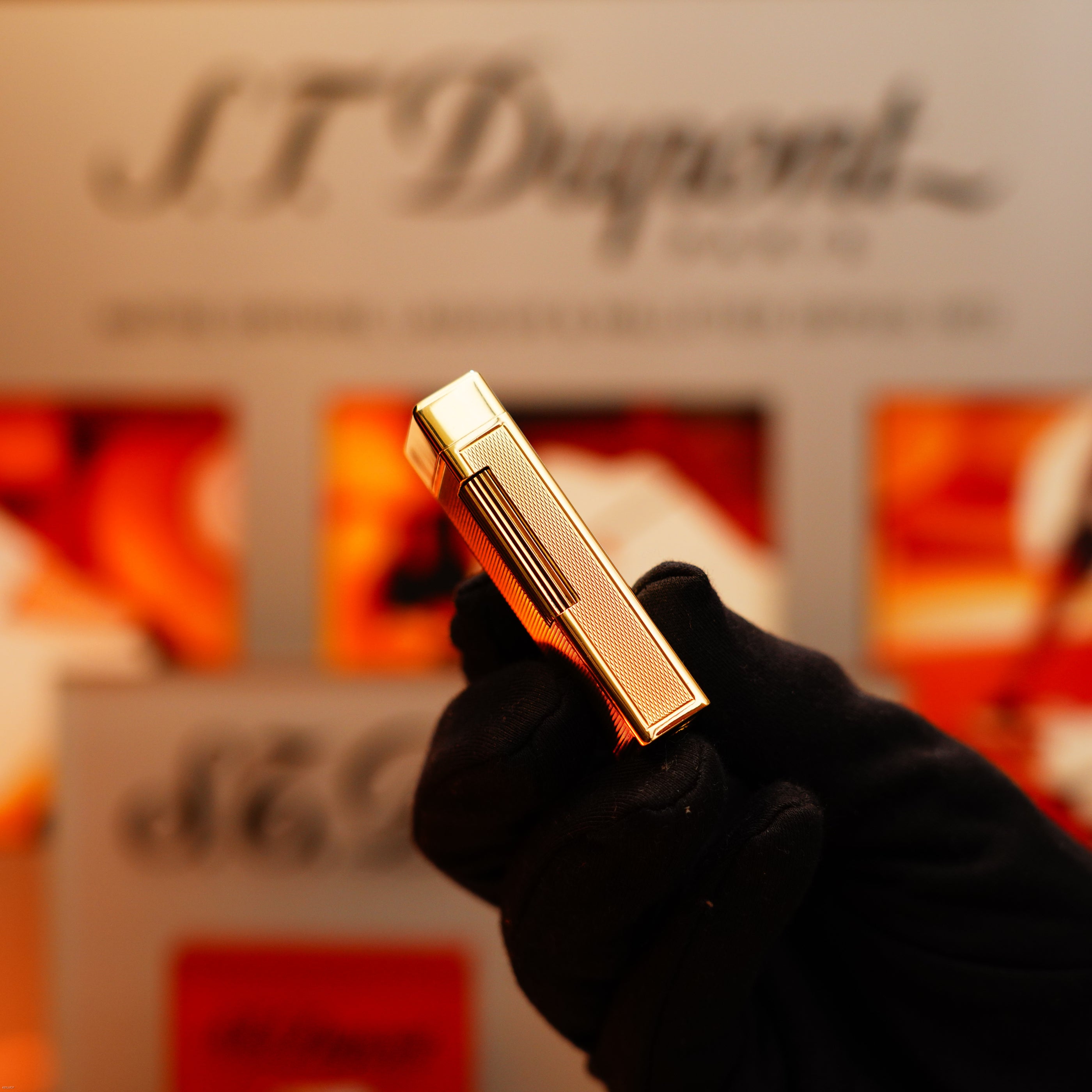 A gloved hand holds a vintage 1964 Dunhill Rollagas lighter in solid 18k gold with a 750 hallmark, its textured surface gleaming against a blurred Dunhill-branded background.