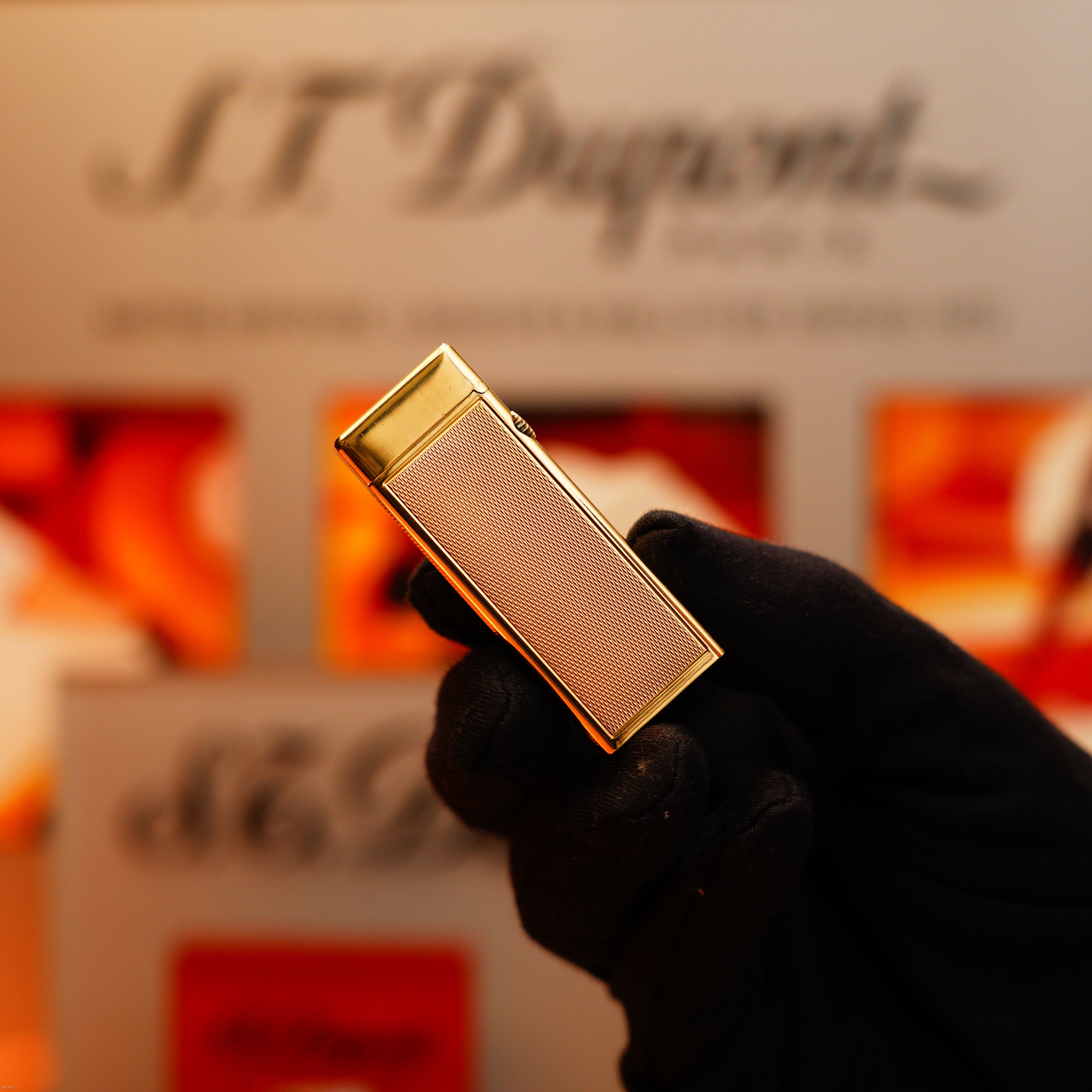 A gloved hand holds a rectangular, solid 18k gold Dunhill Vintage 1964 Oct. Rollagas lighter with a 750 hallmark against a blurred background.