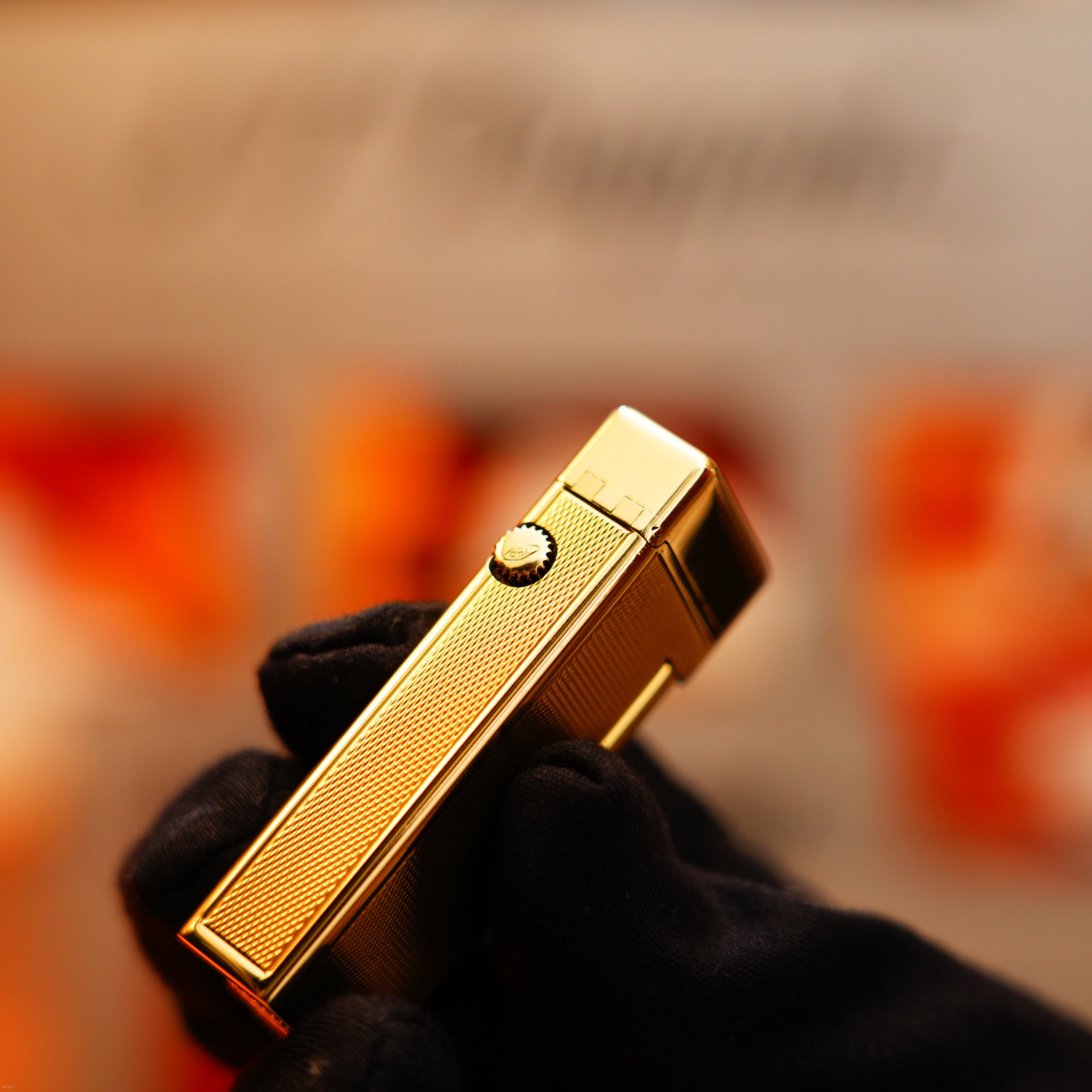 A gloved hand holds a Dunhill Vintage 1964 Oct. Rollagas Early Production Solid 18k Gold Lighter with a 750 hallmark and textured finish against a blurred background.