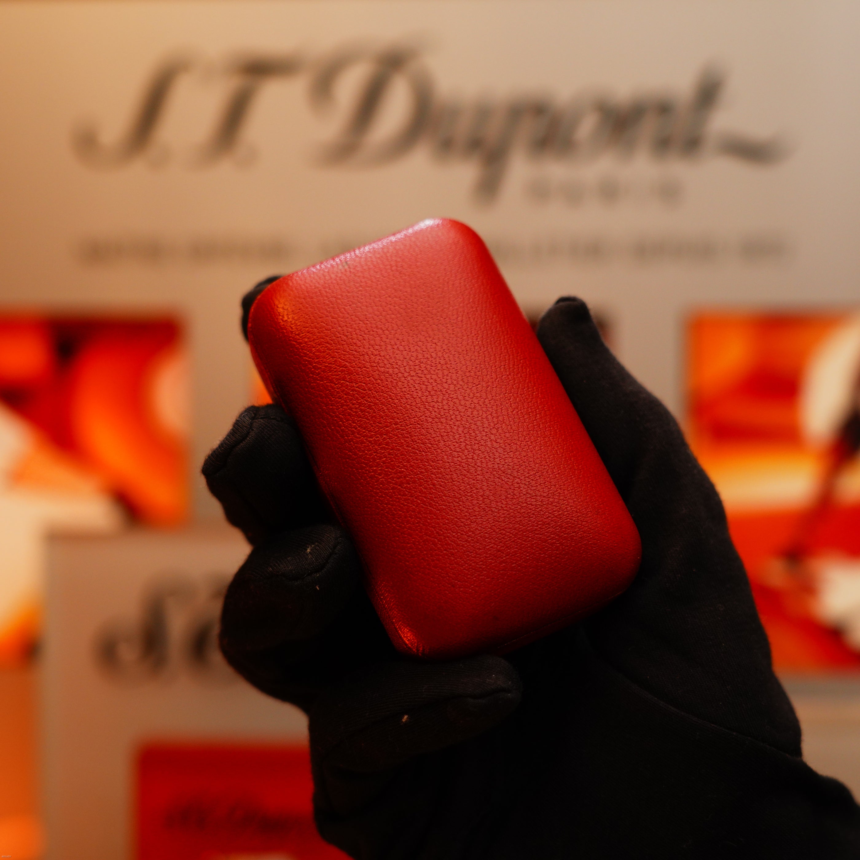 A gloved hand holds a Vintage 1964 Dunhill Rollagas solid 18k gold lighter, stamped with a 750 hallmark, in front of a blurred Dunhill-branded background.