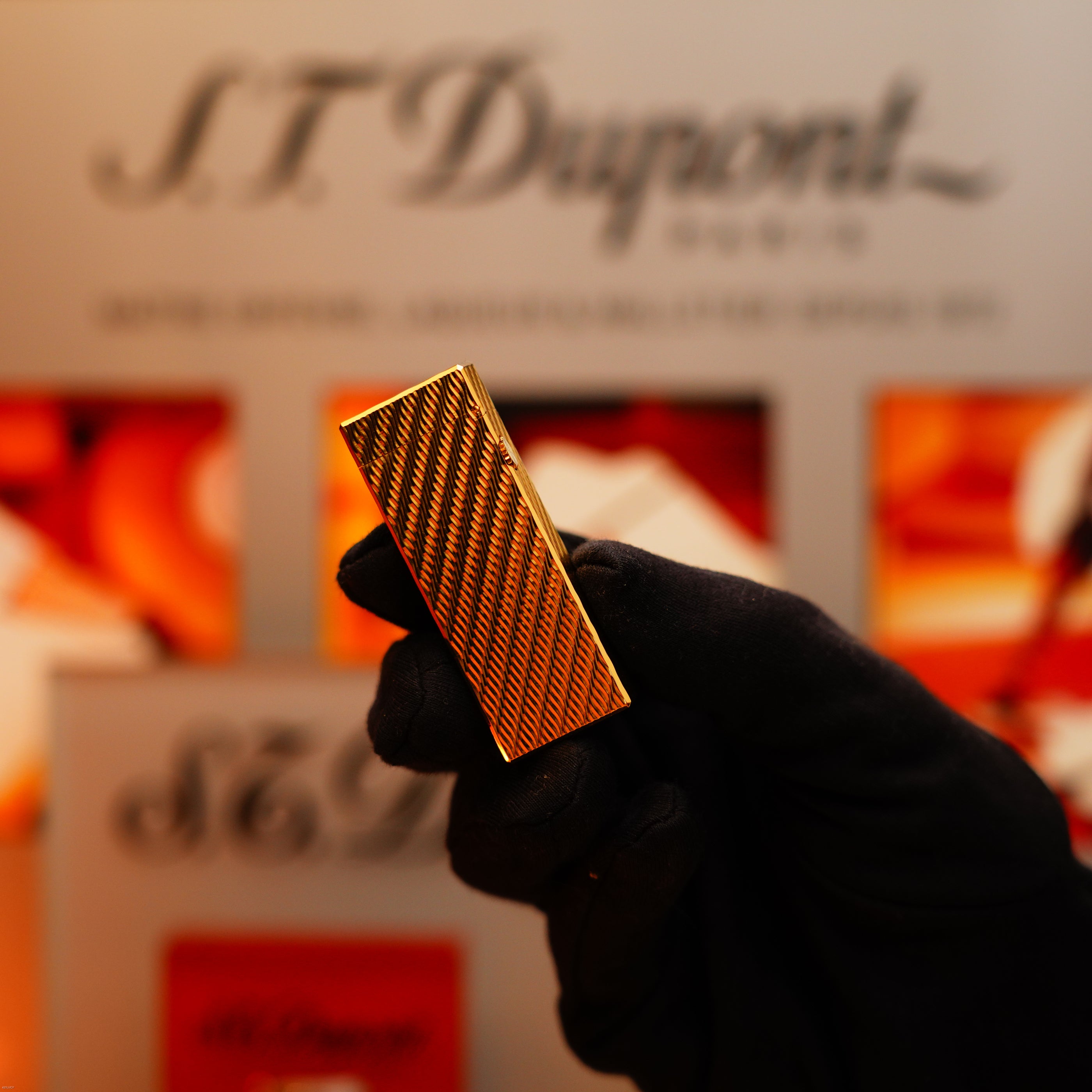 A gloved hand holds a Dunhill Vintage 1971 24k Gold Finish Rollagas lighter with a rare guilloché wave pattern; Dunhill logo and packaging appear blurred in the background.