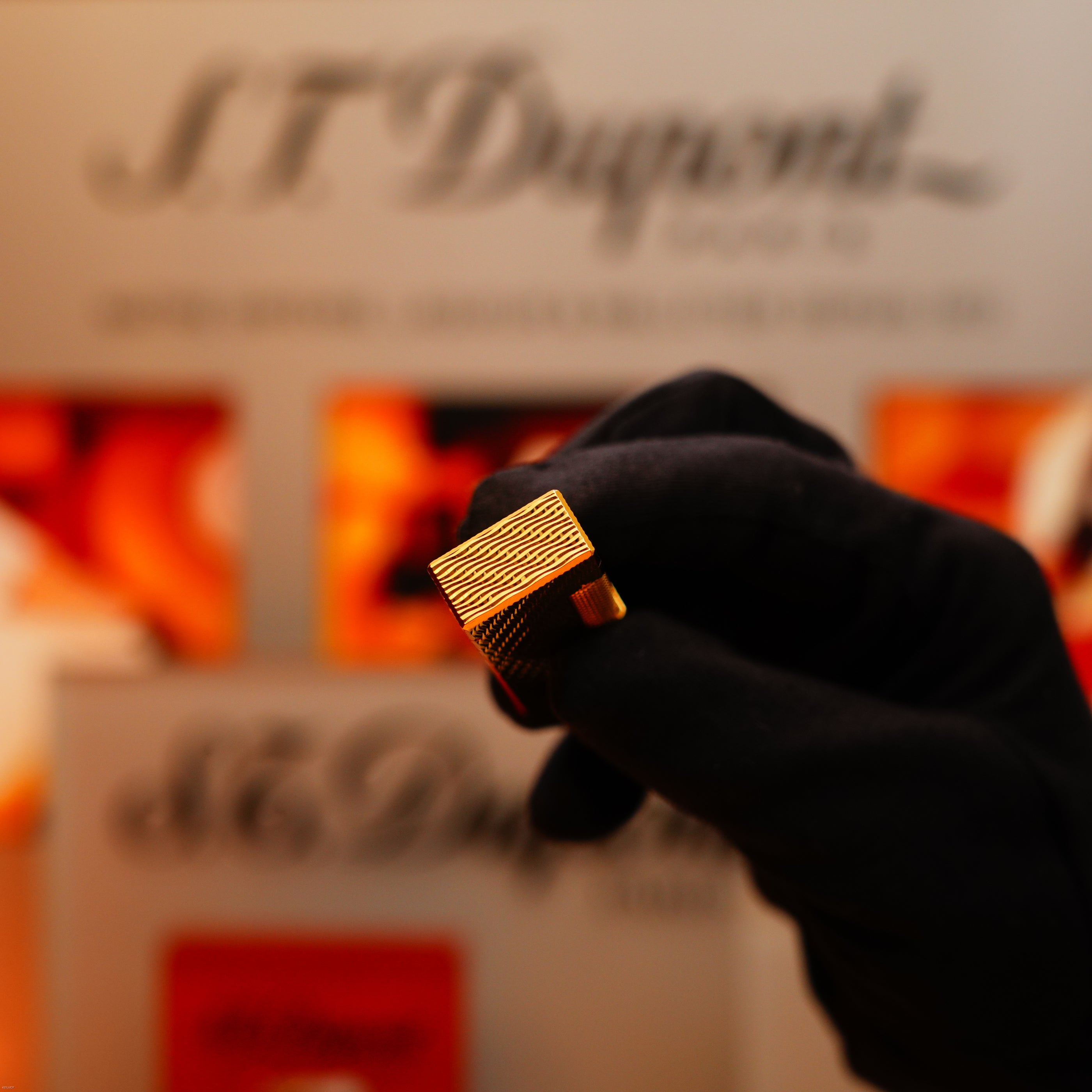 A gloved hand holds a Vintage 1971 Dunhill 24k Gold Finish Rollagas Rare Guilloché Wave Pattern Initial Version Lighter, with blurred Dunhill branding in the background.