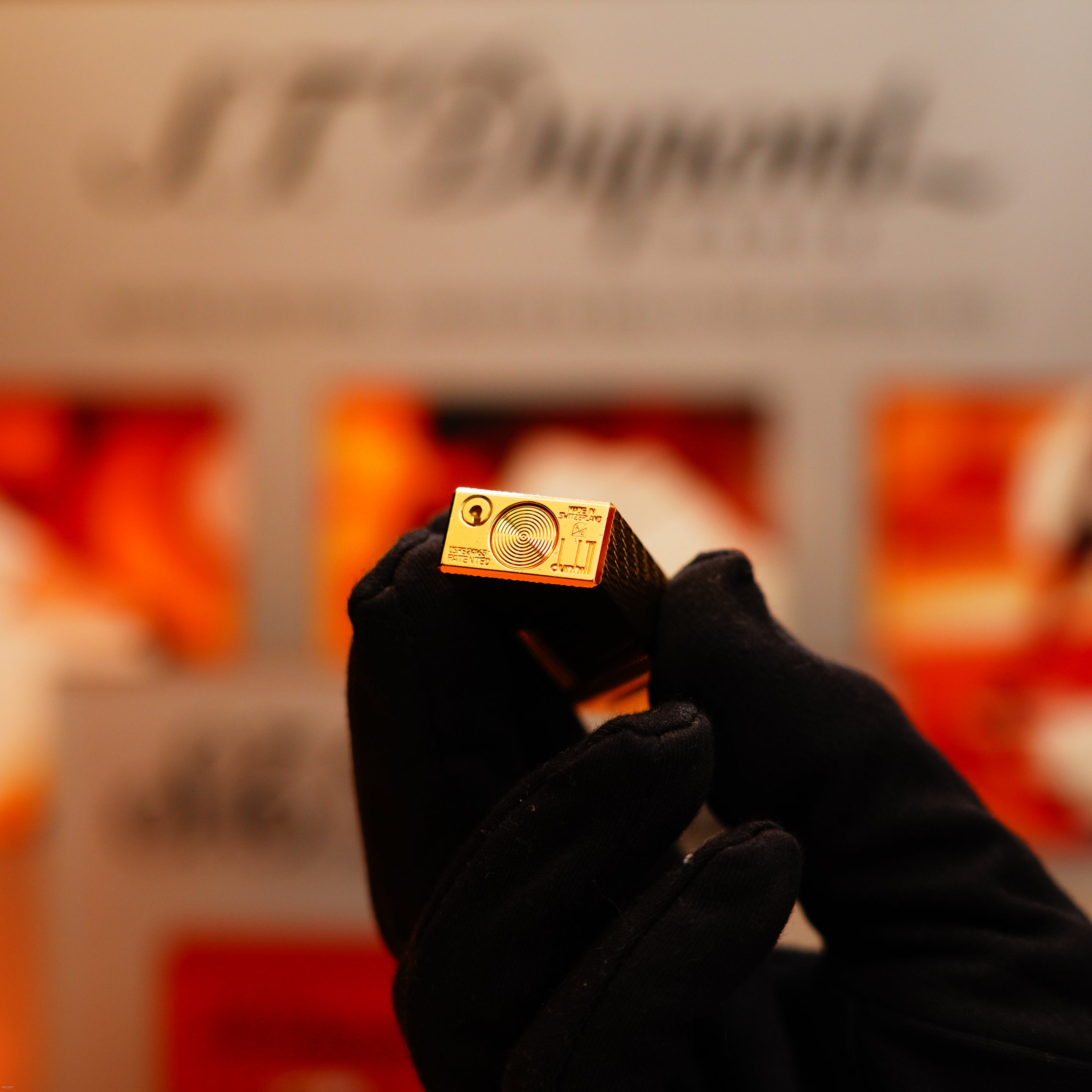 A gloved hand holds up a Vintage 1971 Dunhill 24k Gold Finish Rollagas Rare Visual Guilloché Wave Pattern Initial Version Lighter, set against a blurred background with the Dunhill logo.