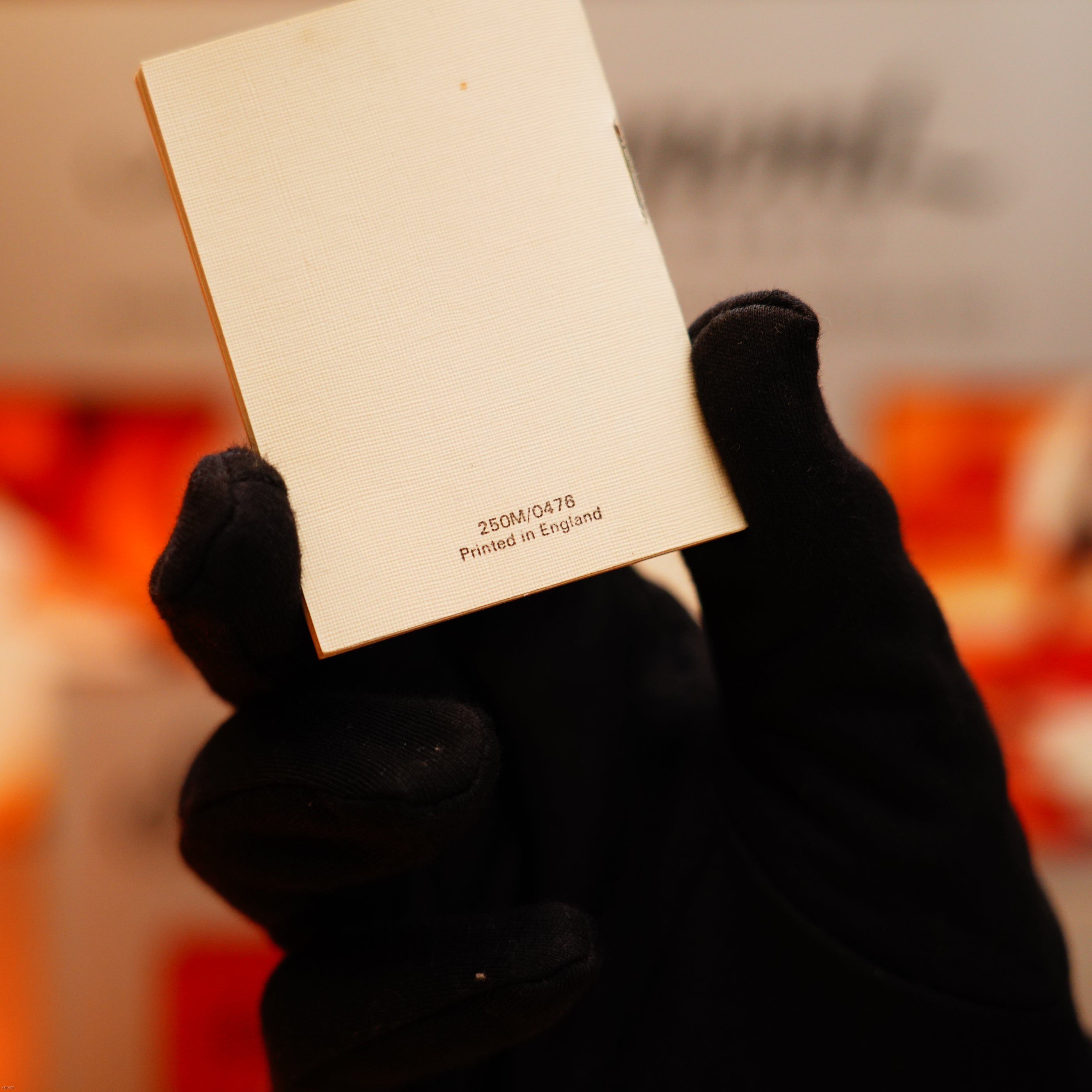 A gloved hand holds a small white card with "250M/0476 Printed in England" on the back, accompanying a Vintage 1971 Dunhill 24k Gold Finish Rollagas Rare Visual Guilloché Wave Pattern Initial Version Lighter.