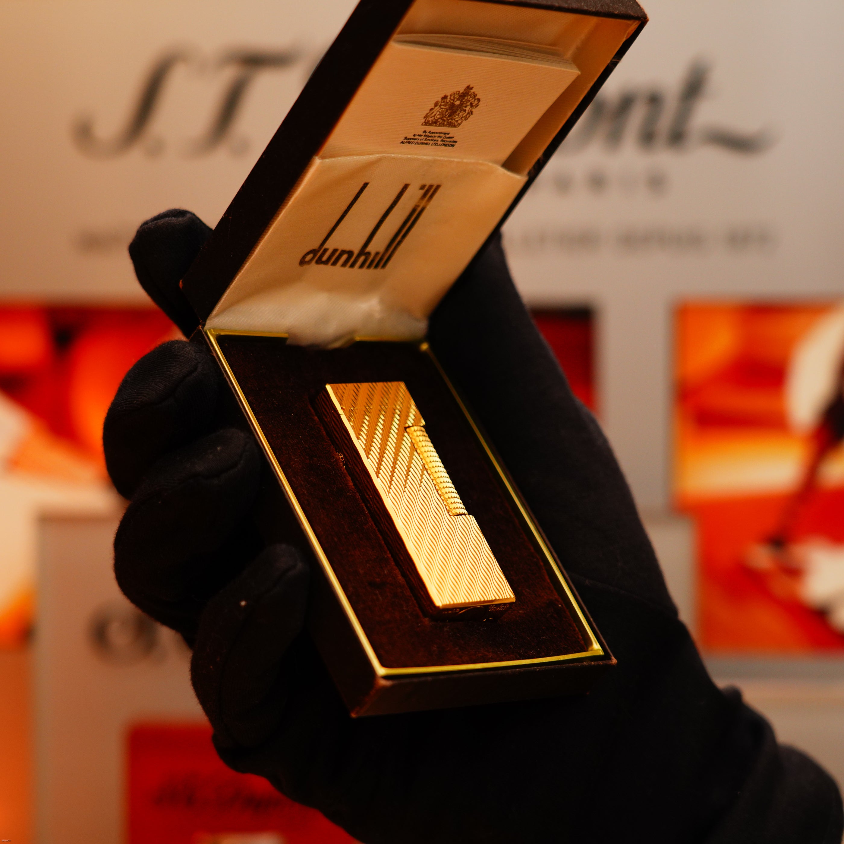 A gloved hand holds an open box displaying a Vintage 1971 Dunhill 24k Gold Finish Rollagas Lighter with rare Visual Guilloché Wave Pattern, set against a blurred background.