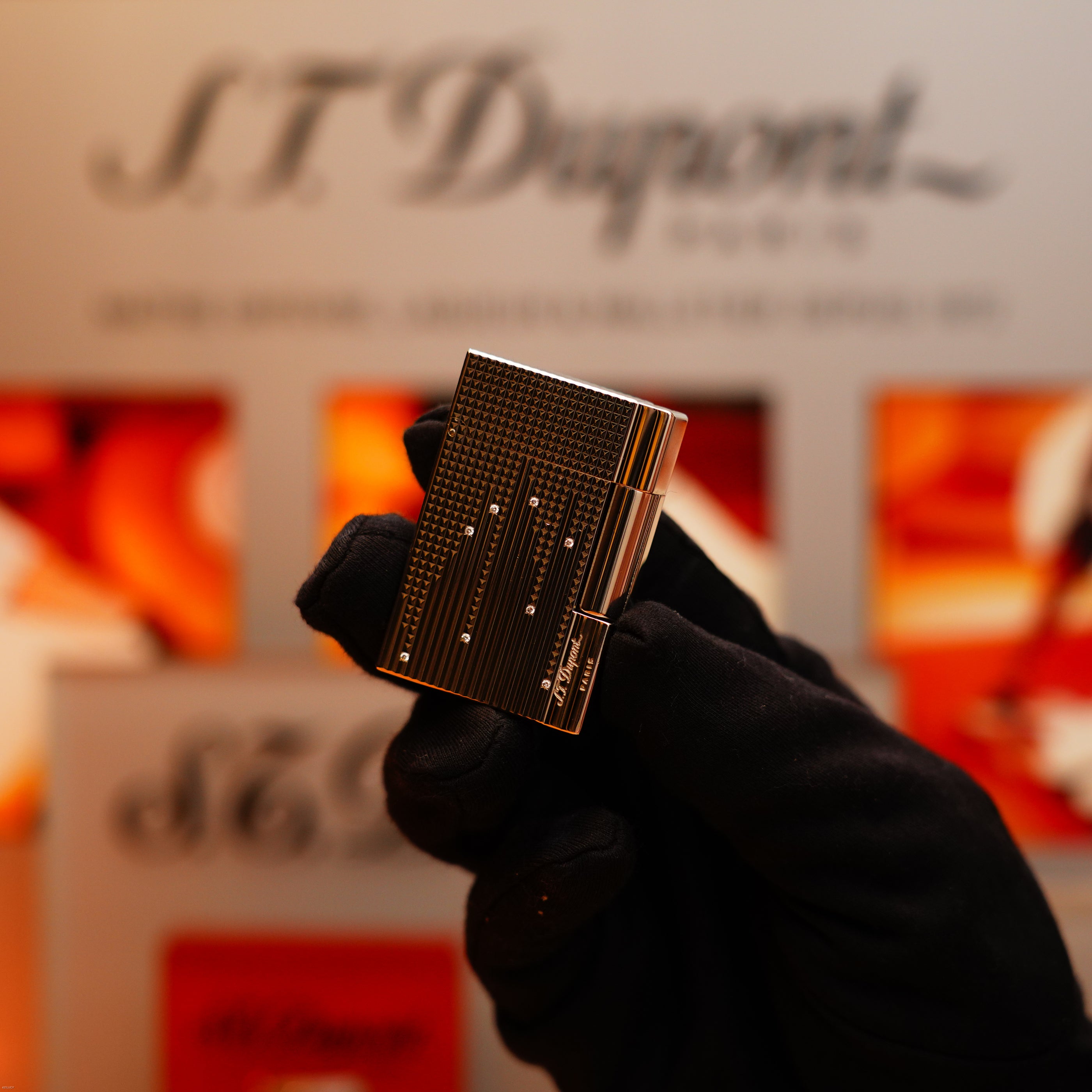 A gloved hand holds a Vintage 2005 S.T. Dupont Gatsby Diamond Drops with 16 Natural Diamond Heavy Platinum Limited Edition Lighter, displayed against an S.T. Dupont branded background.
