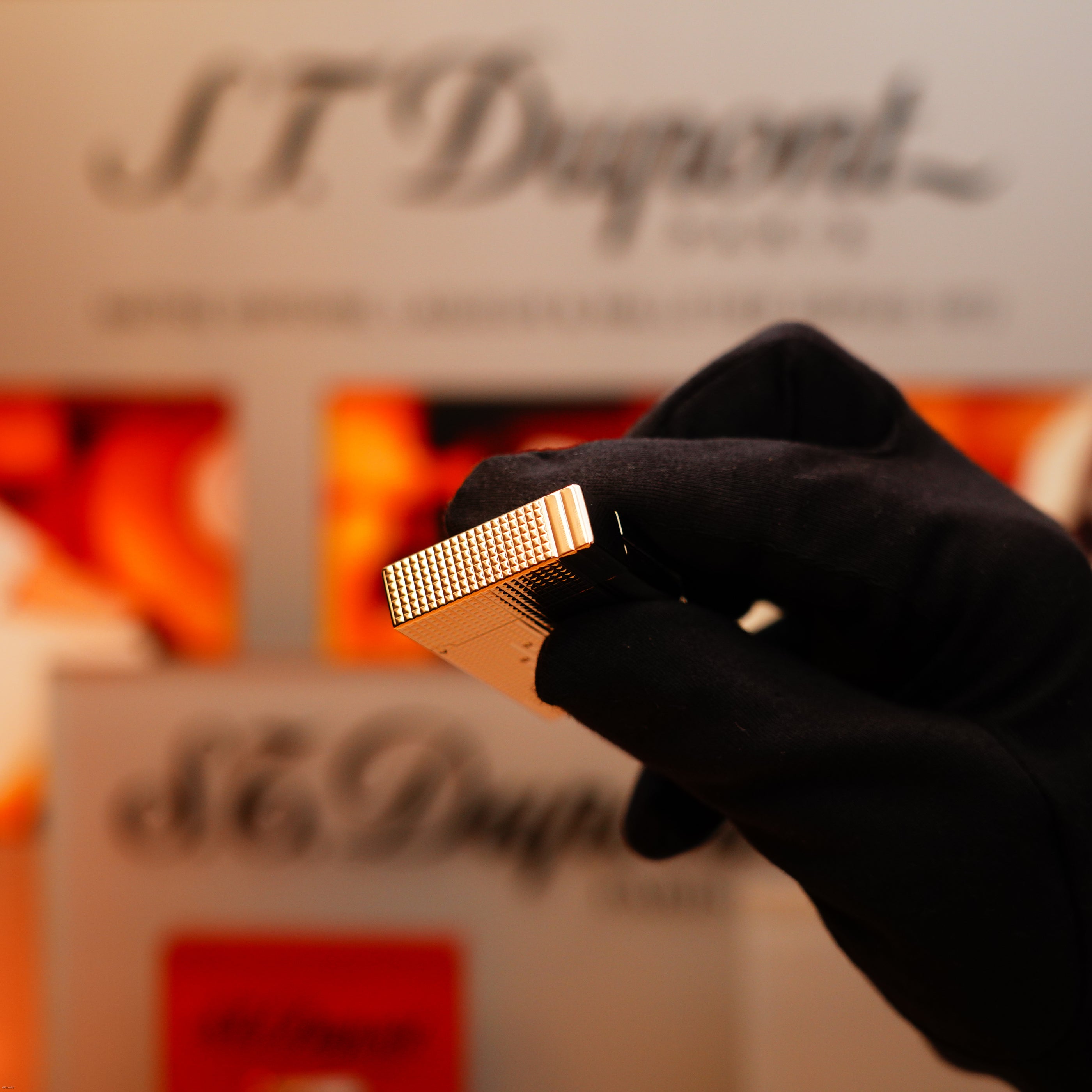 A gloved hand holds a Vintage 2005 S.T. Dupont Gatsby Diamond Drops with 16 Natural Diamond Heavy Platinum Limited Edition Lighter before a blurred background featuring the S.T. Dupont logo and packaging.