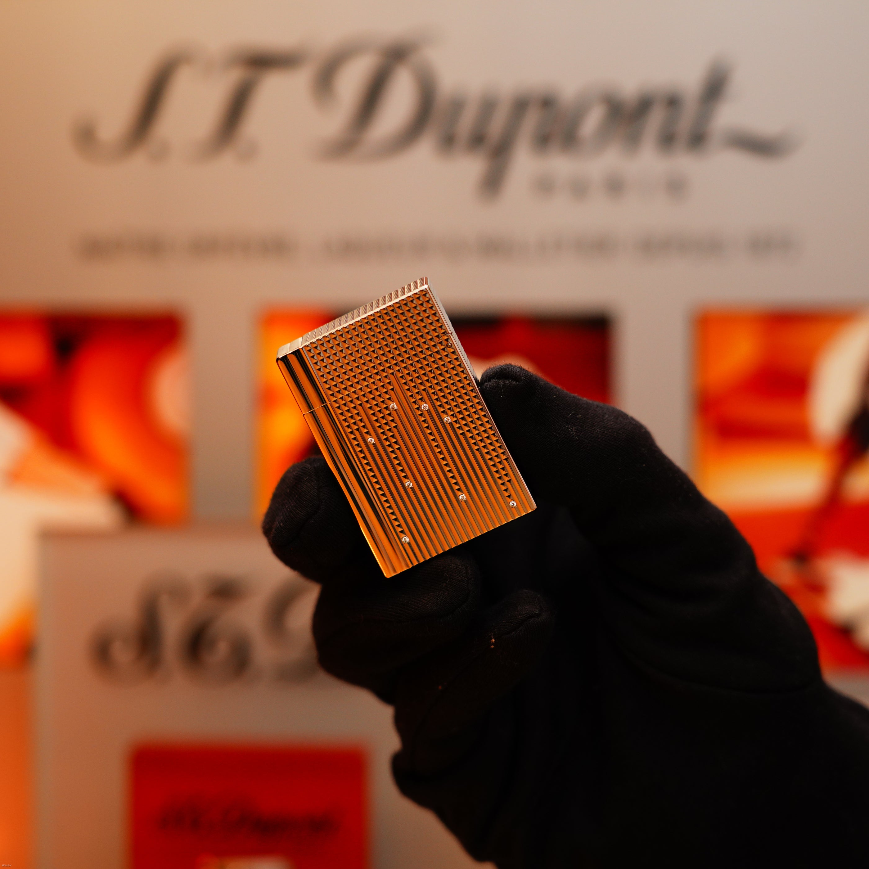 A gloved hand holds a Vintage 2005 S.T. Dupont Gatsby Diamond Drops Limited Edition Lighter with 16 natural diamonds and heavy platinum finish; branded packaging is blurred in the background.