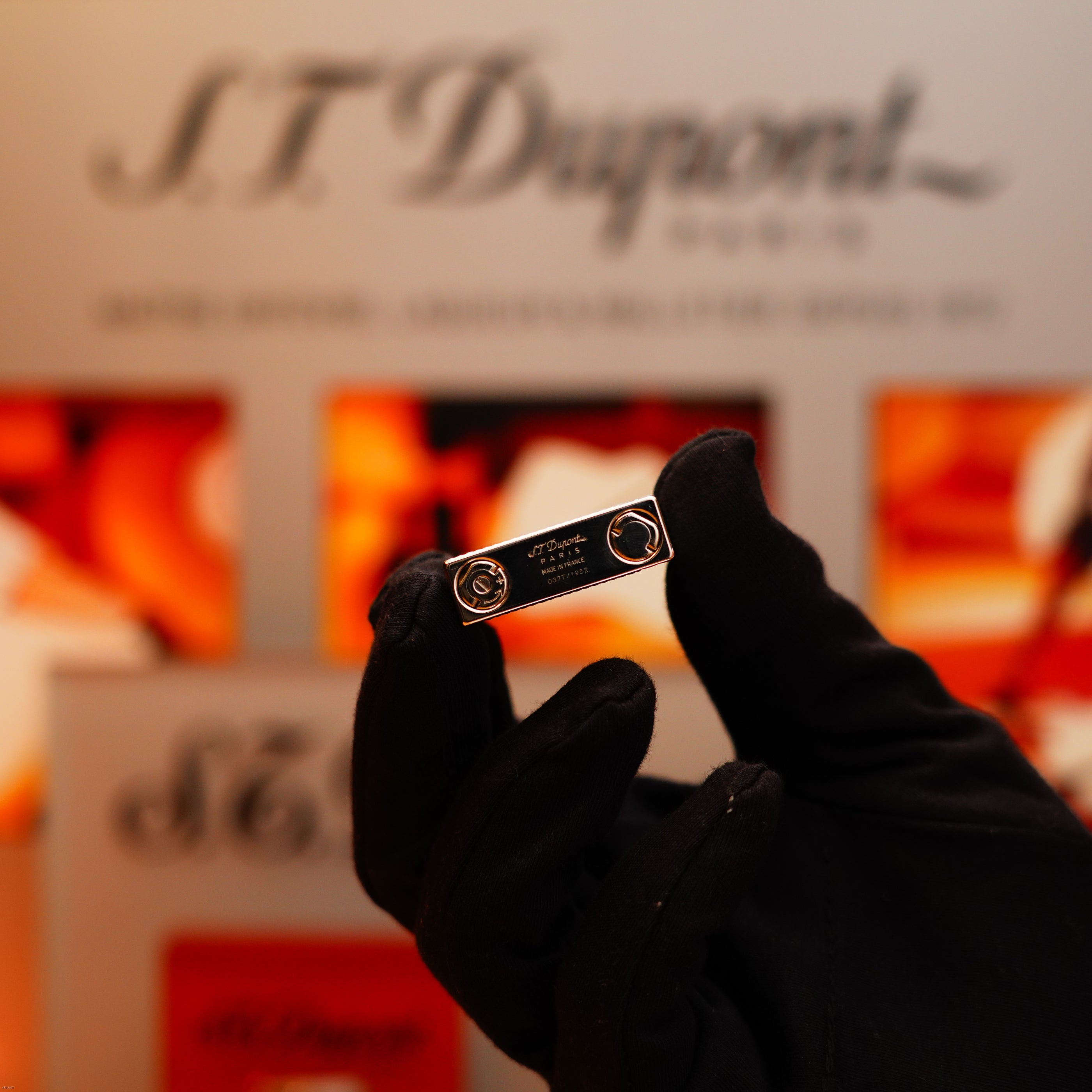A gloved hand holds a Vintage 2005 S.T. Dupont Gatsby Diamond Drops Platinum Limited Edition Lighter, featuring 16 natural diamonds, with a blurred S.T. Dupont display visible in the background.