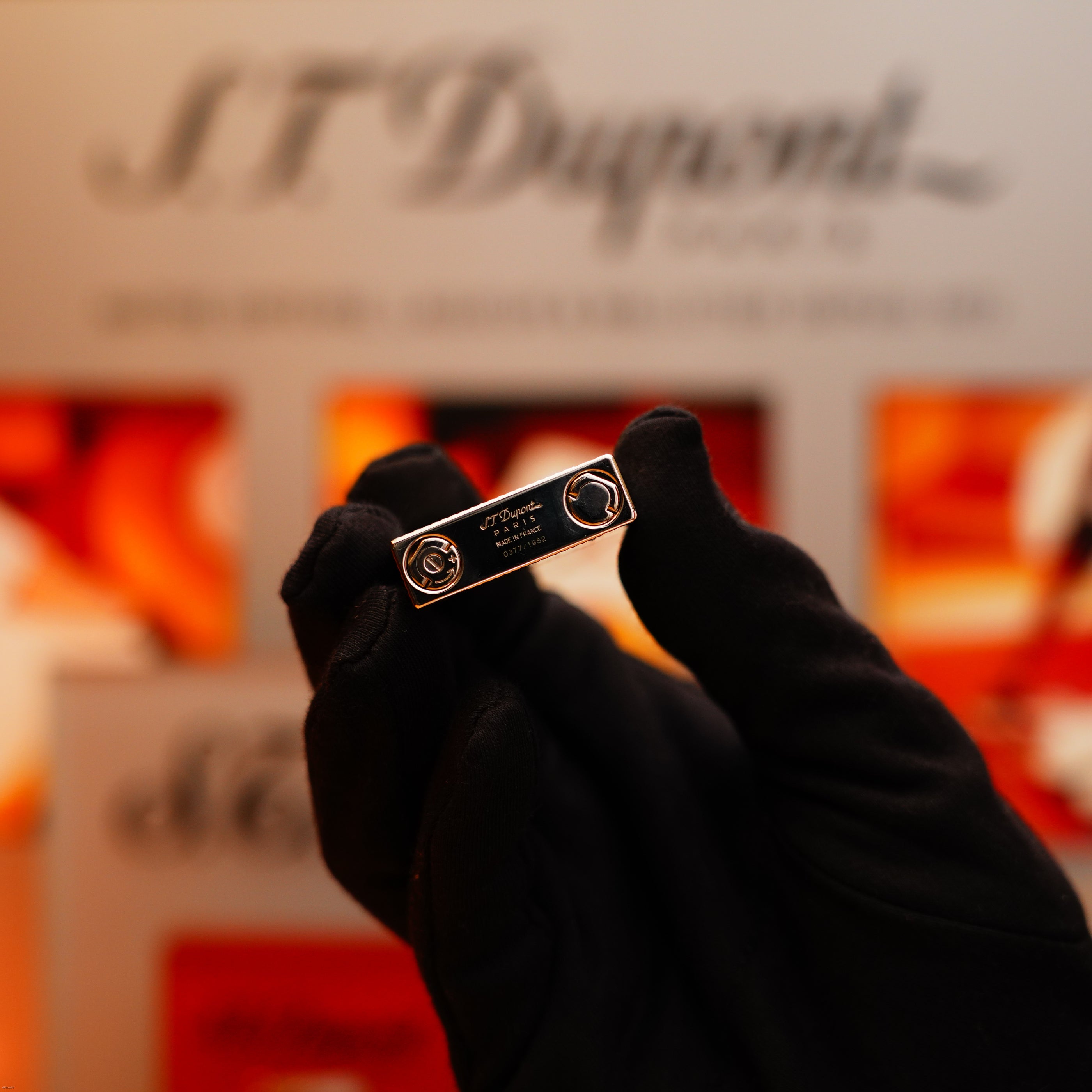 A gloved hand holds the Vintage 2005 S.T. Dupont Gatsby Diamond Drops Limited Edition Lighter, featuring 16 natural diamonds and engraved details, with a blurred background displaying the S.T. Dupont logo.