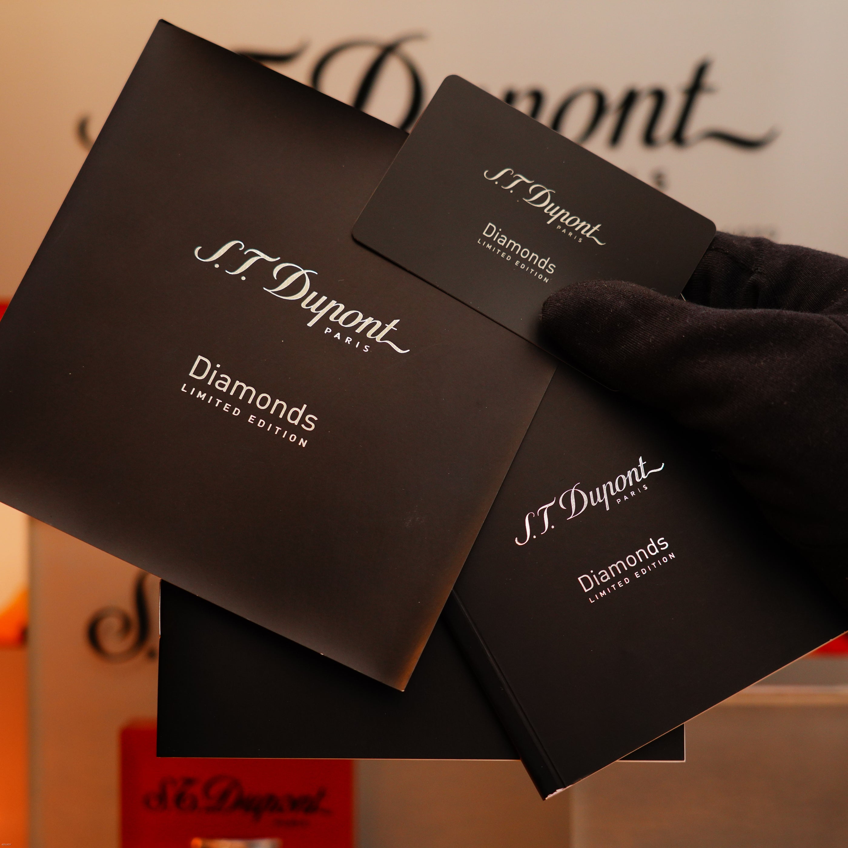 A gloved hand holds S.T. Dupont branding, displaying the Vintage 2005 St Dupont Gatsby Diamond Drops with 16 Natural Diamond Heavy Platinum Limited Edition Lighter packaging and a card against a blurred background.