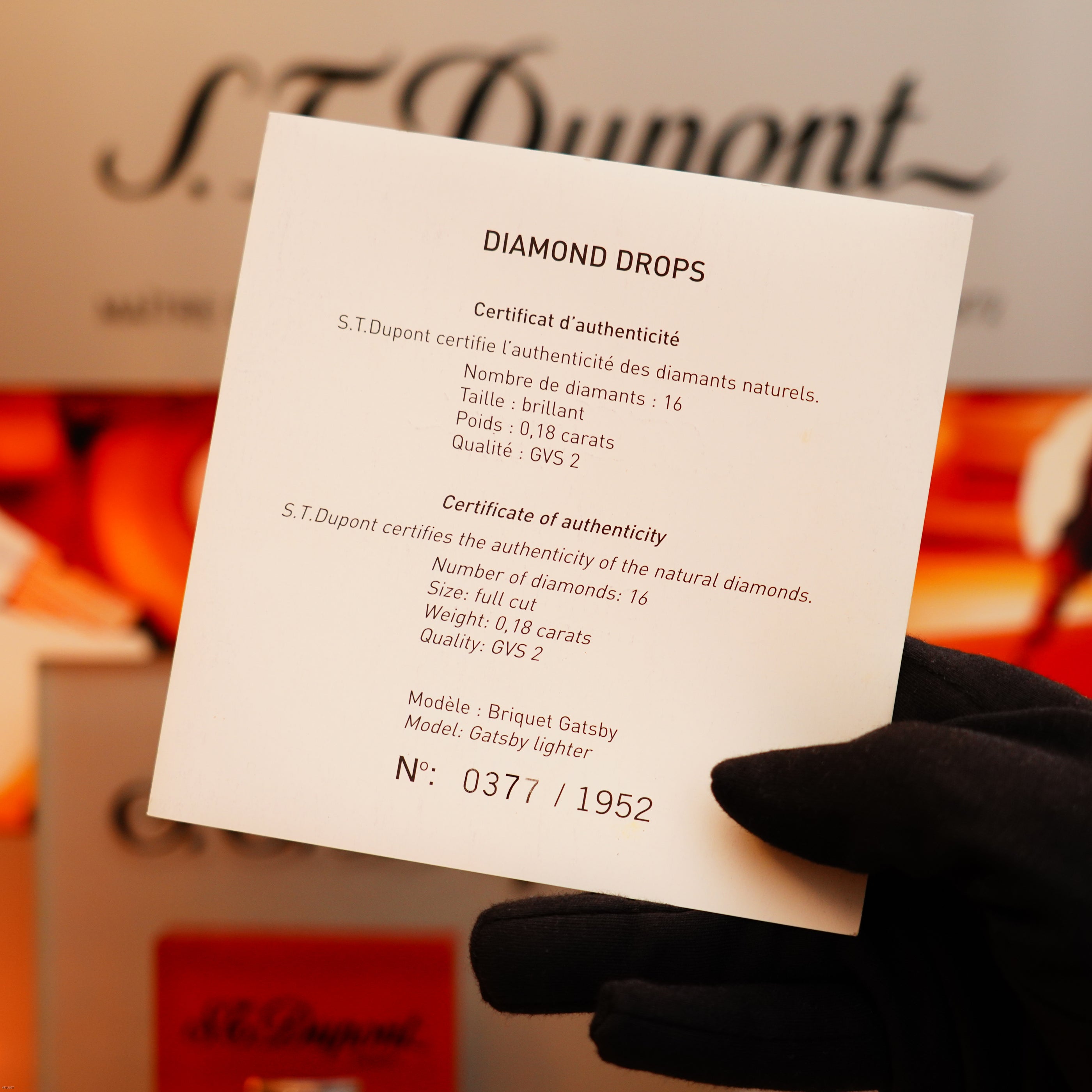 A gloved hand holds a certificate of authenticity for the S.T. Dupont Vintage 2005 Gatsby Diamond Drops Limited Edition Lighter, confirming 16 natural diamonds (0.18 ct) and heavy platinum, numbered 0377/1952.