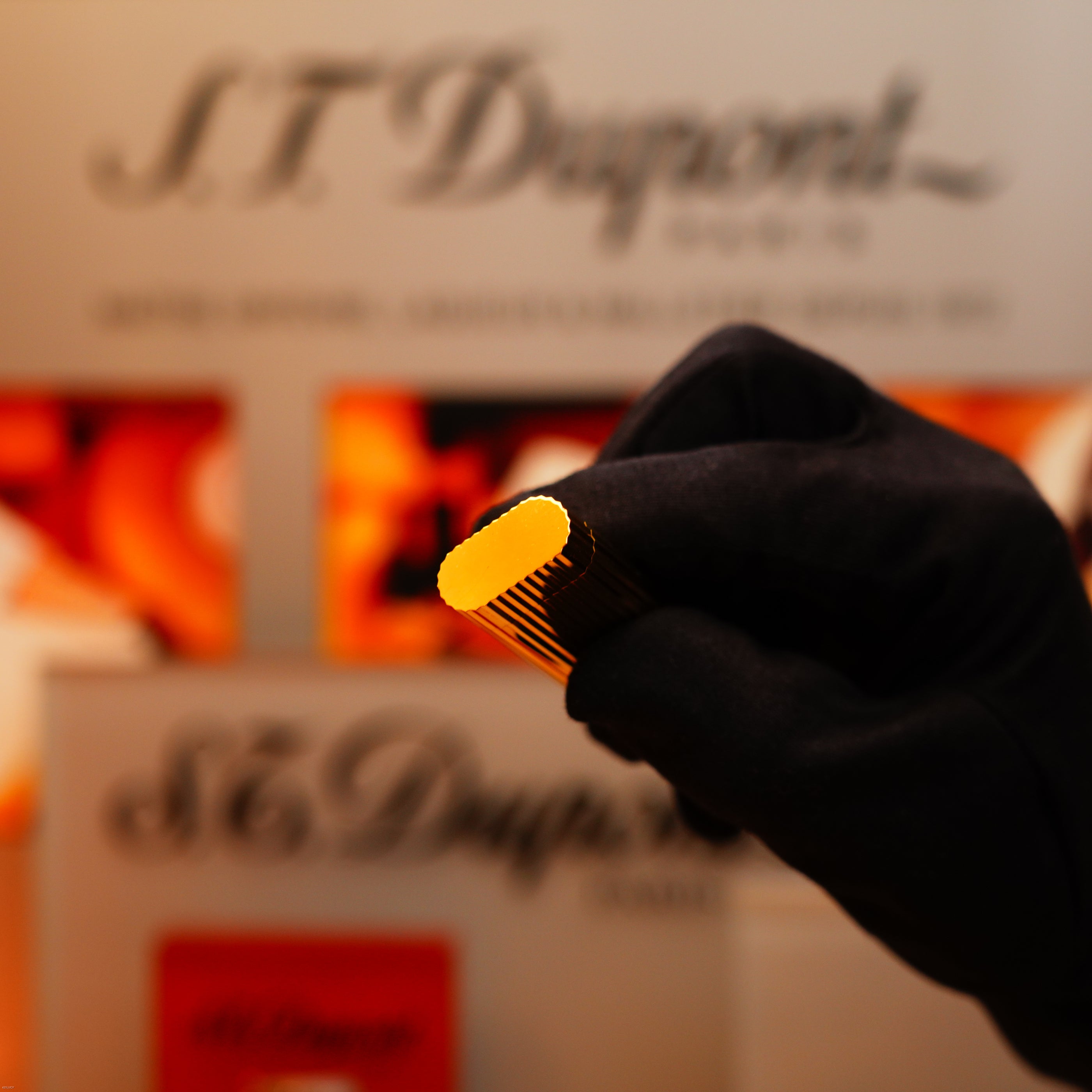 A gloved hand holds a Vintage 1980 Cartier Vertical line Heavy 24k Gold Finish Oval Le Must Lighter in front of a blurred Cartier-branded background.