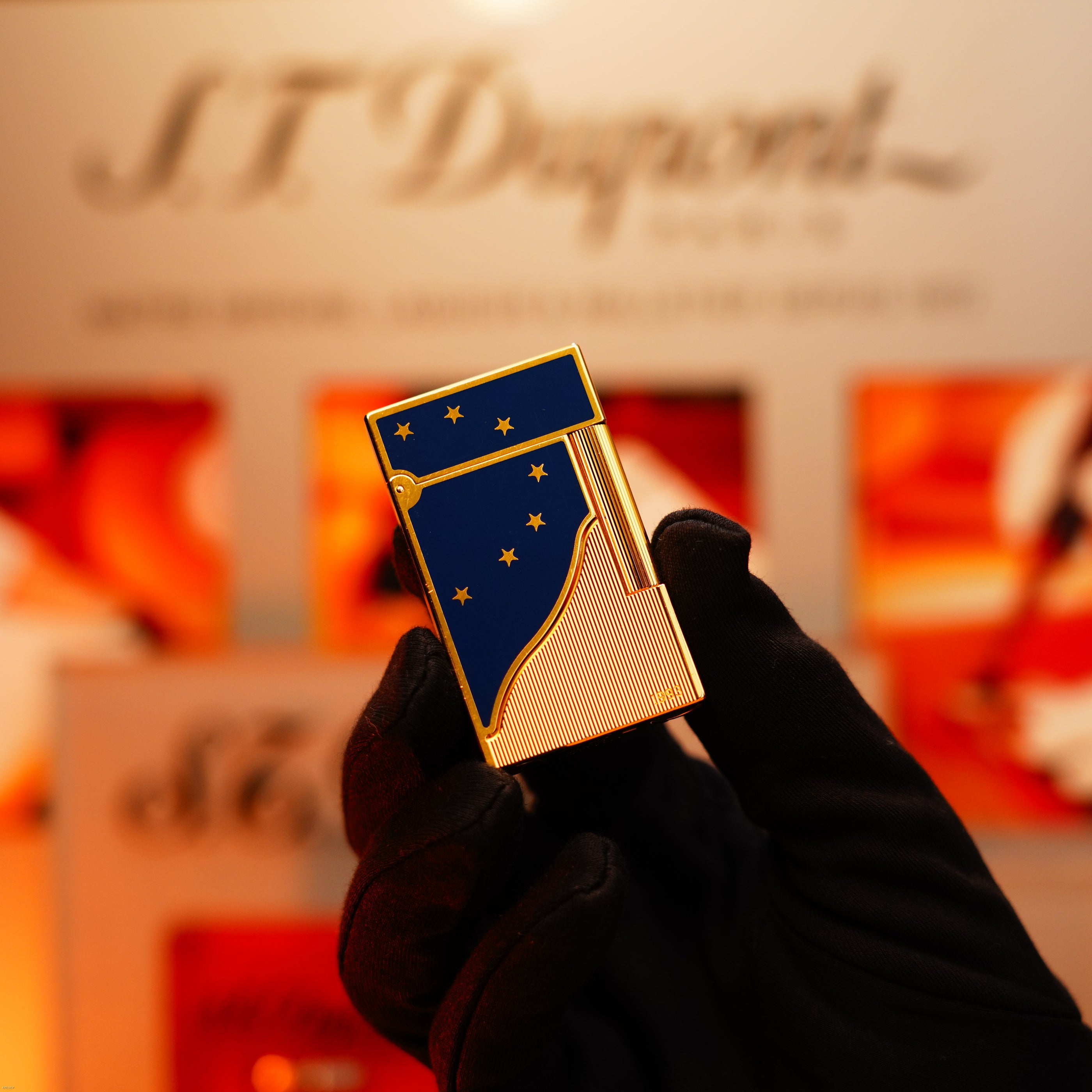 A gloved hand holds the Vintage 1993 Lucy Lighter Europe Rare 24k Gold Finish Blue Lacquer Limited Edition Ligne 2, in front of a blurred S.T. Dupont display.