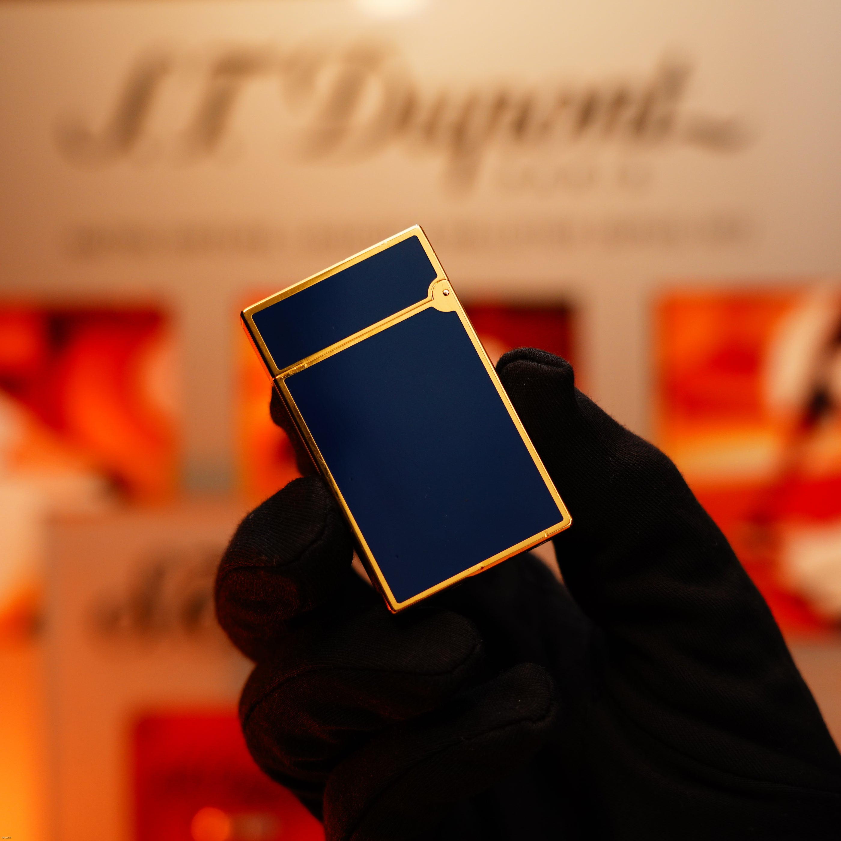 A hand in a black glove holds a Vintage 1993 St Dupont Europe Rare 24k Gold Finish Blue Lacquer Limited Edition Ligne 2 Lighter by Lucy Lighter—an elegant piece noted for quality repair and warranty options, against a blurred background.