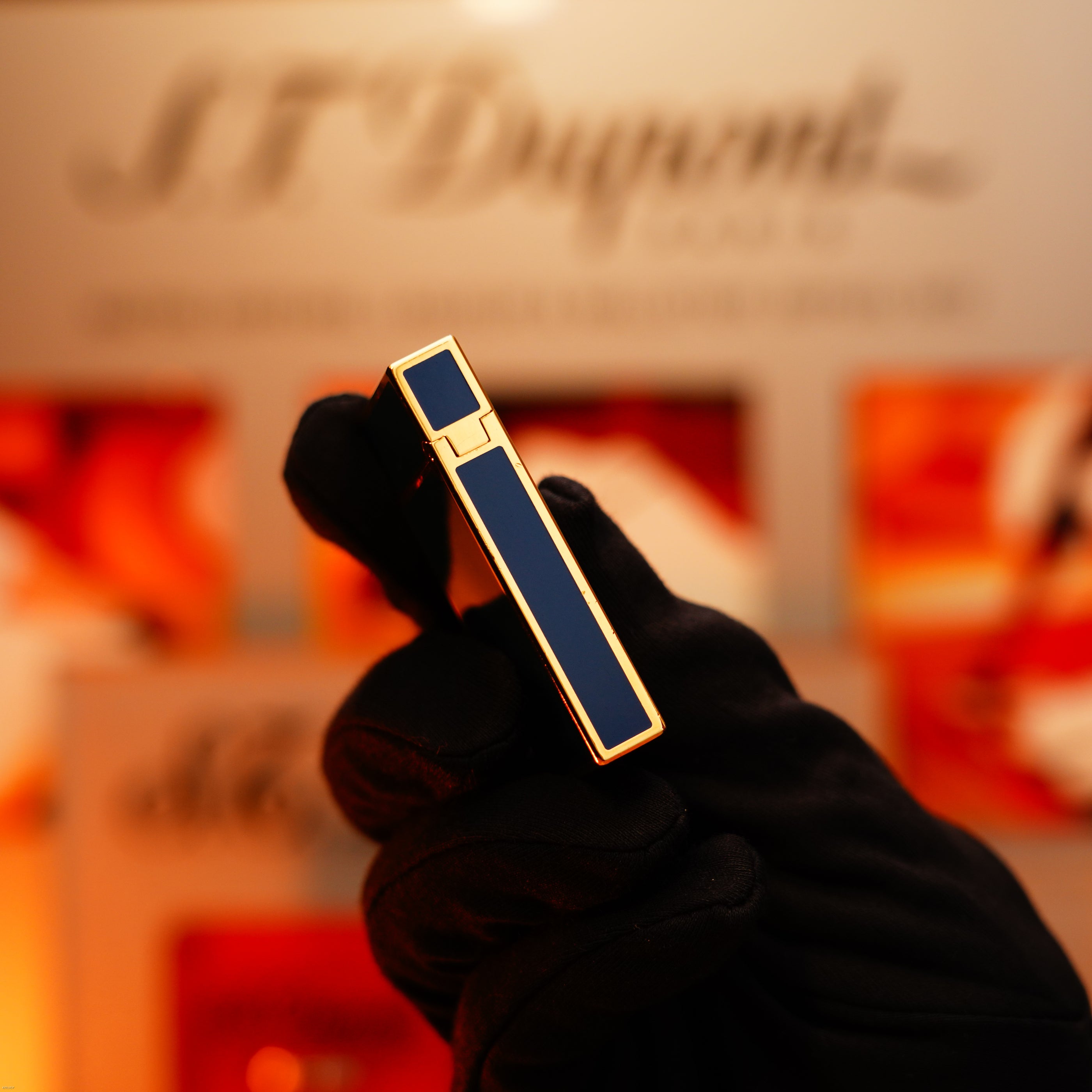 A gloved hand holds a Vintage 1993 Lucy Lighter Rare 24k Gold Finish Blue Lacquer Limited Edition Ligne 2, with a blurred branded background.