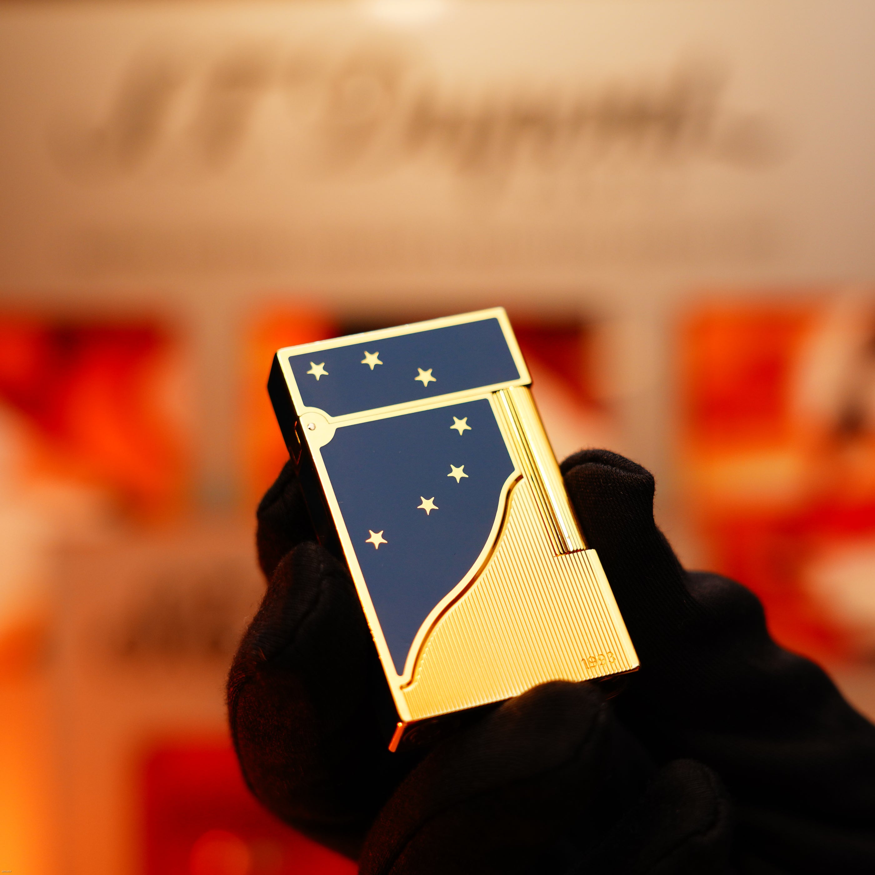 A gloved hand holds the Lucy Lighter Vintage 1993 St Dupont Europe Rare 24k Gold Finish Blue Lacquer Limited Edition Ligne 2 Lighter, showcased against a blurred, warmly toned background.