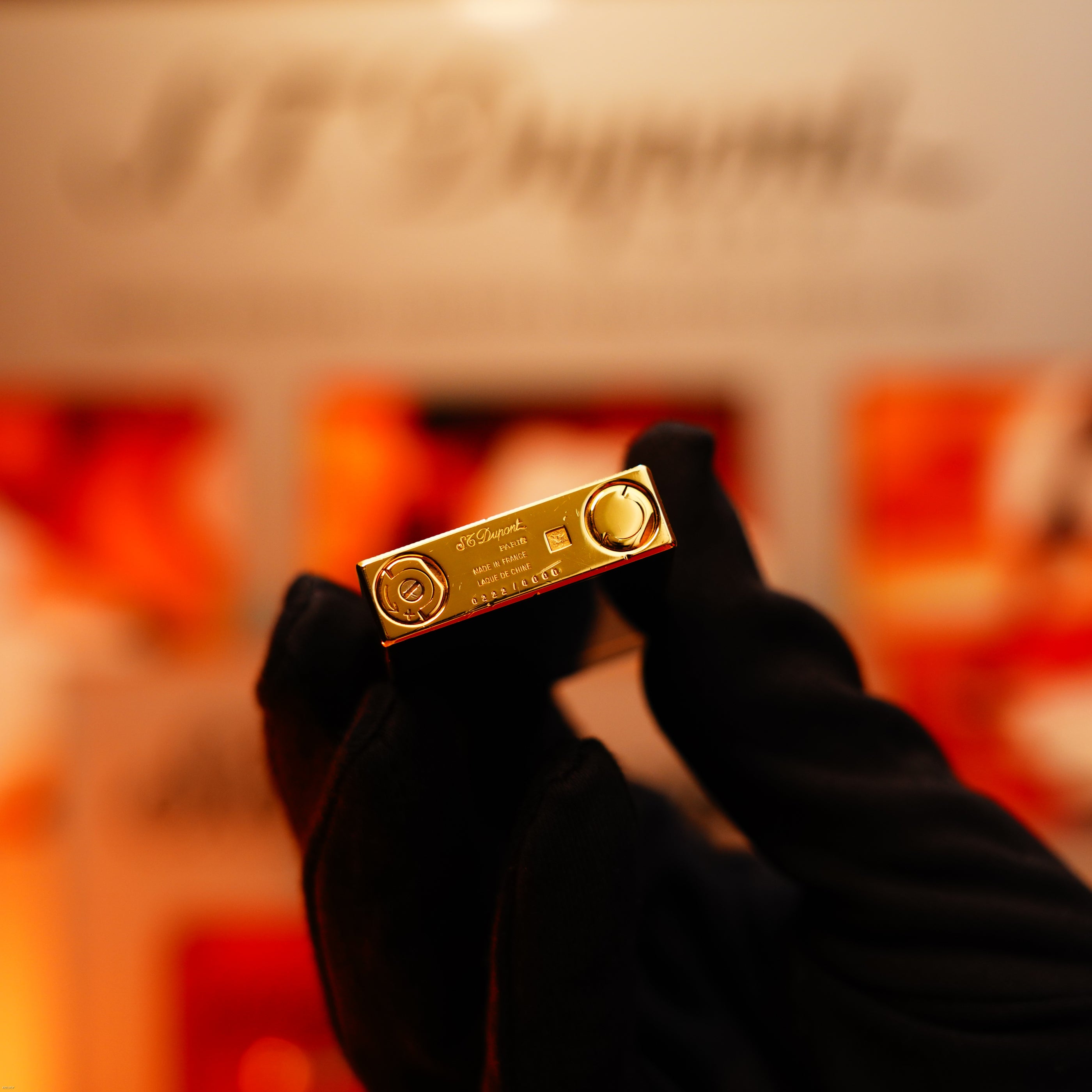 A gloved hand holds a Vintage 1993 Lucy Lighter Ligne 2, a rare limited edition with 24k gold finish and blue lacquer, showing engraved branding and bottom details against a blurred background.