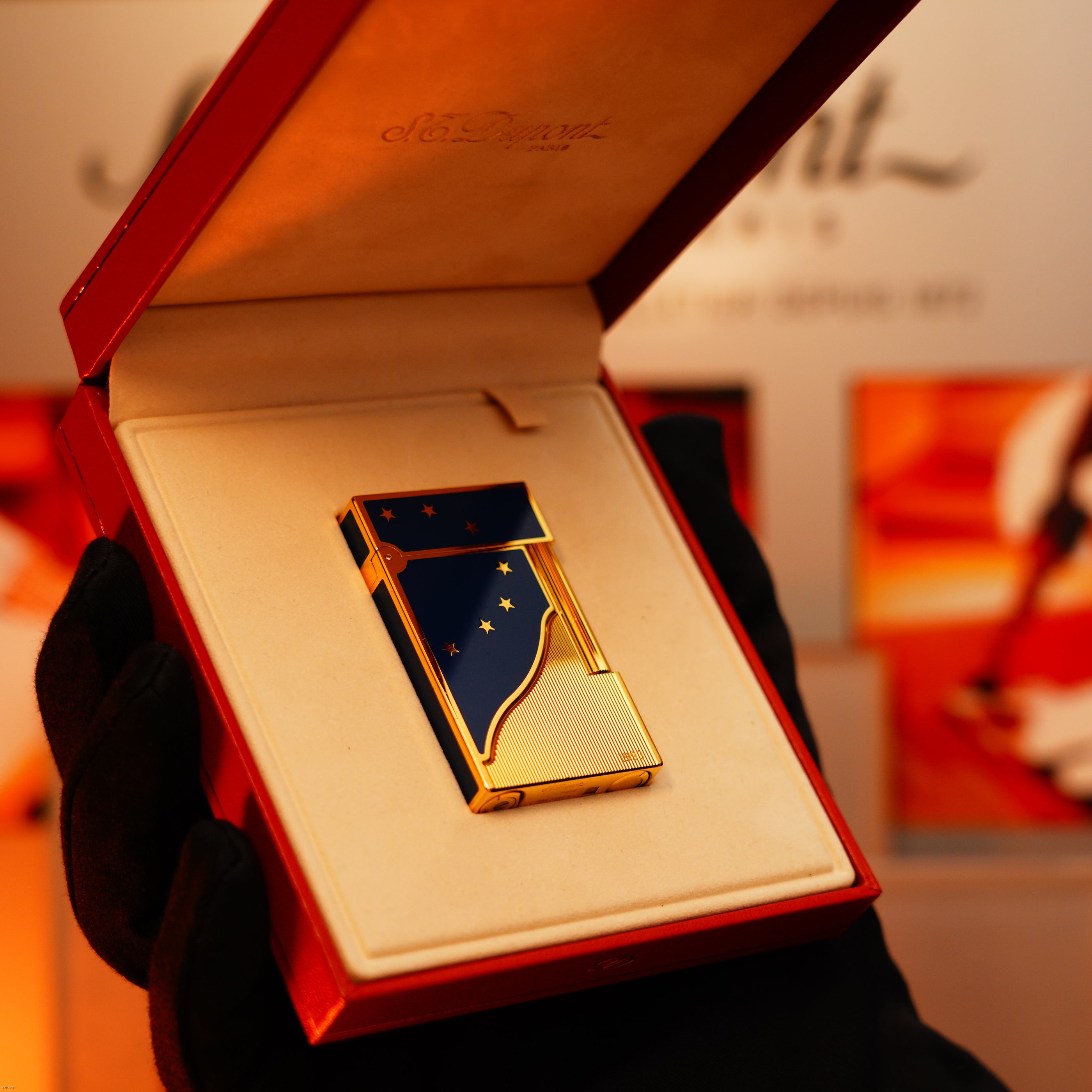 A gloved hand holds an open red box displaying the rare Vintage 1993 St Dupont Europe 24k Gold Finish Blue Lacquer Limited Edition Ligne 2 Lighter by Lucy Lighter, set in a cream interior—an elegant collectible often with repair and warranty options.