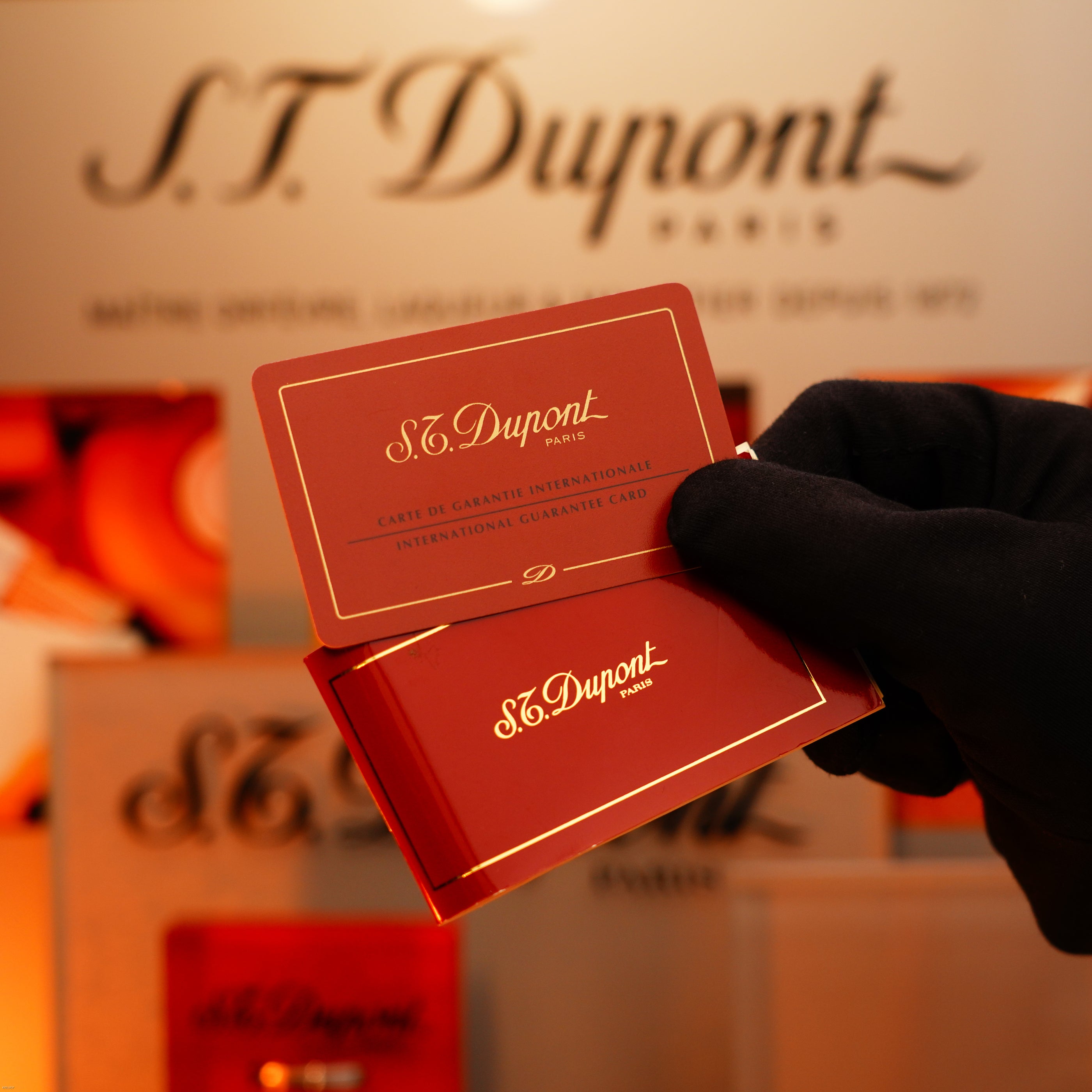 A gloved hand holds Lucy Lighter warranty cards before a branded display, showcasing the assurance and prestige of each Vintage 1993 St Dupont Europe Rare 24k Gold Finish Blue Lacquer Limited Edition Ligne 2 Lighter.