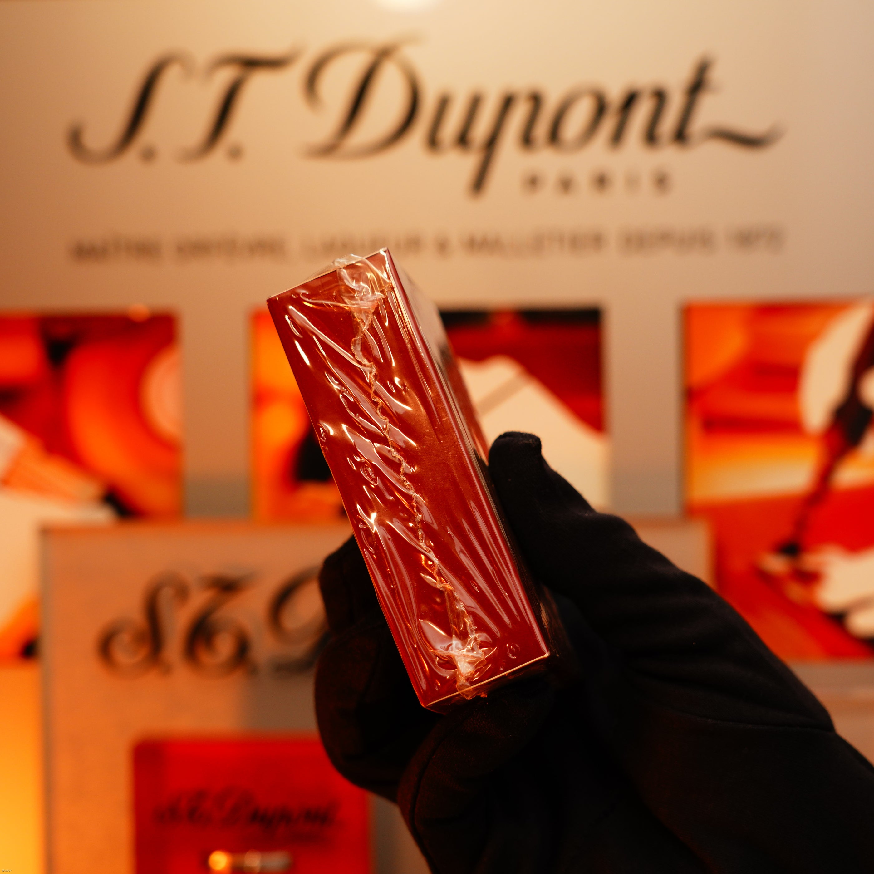 A gloved hand displays a Vintage 1990 Lucy Lighter Heavy Silver iconic Vertical ligne rare Sealed Lighter in a red box, in front of an S.T. Dupont Paris display.
