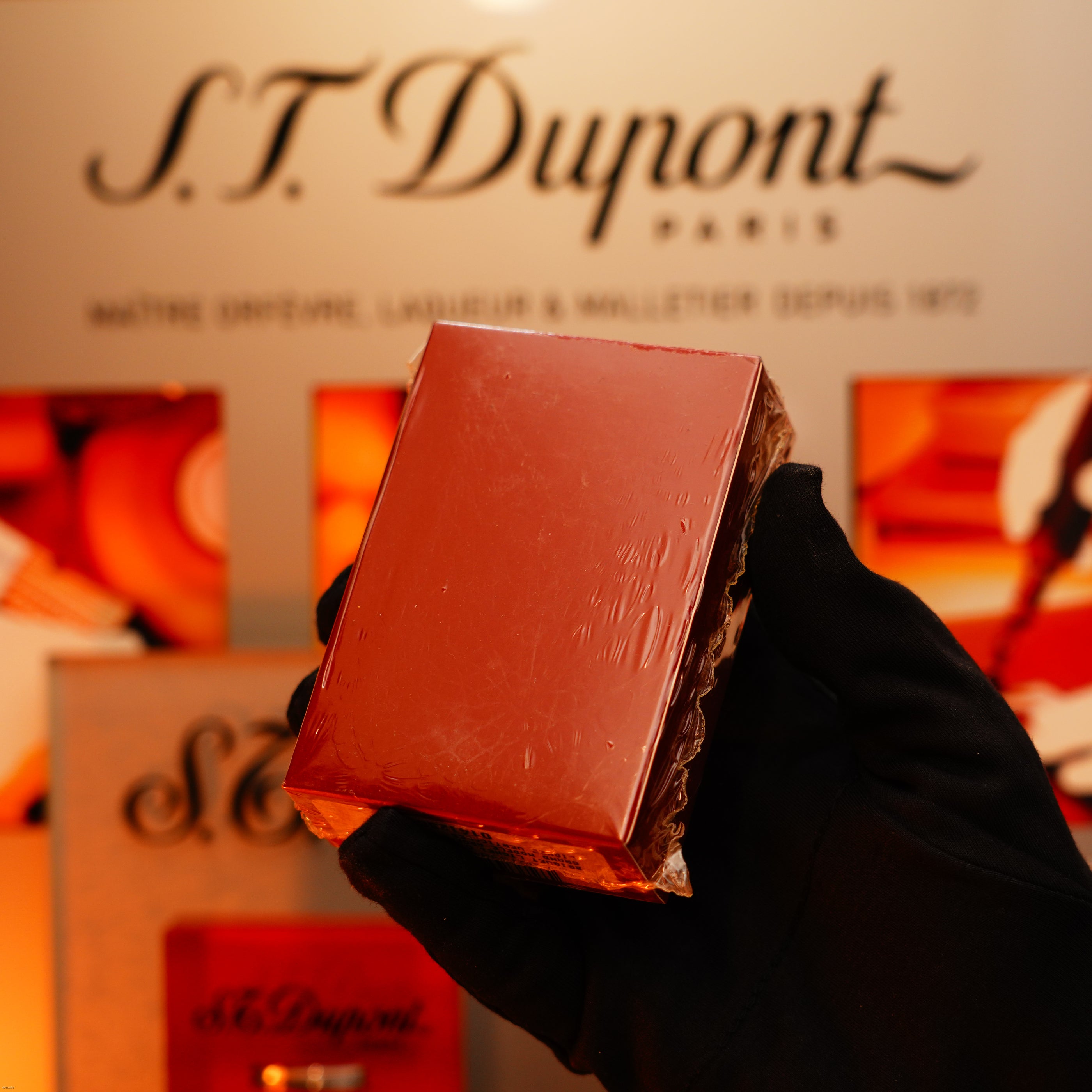 A gloved hand holds a Vintage 1990 St Dupont Heavy Silver iconic Vertical ligne rare Sealed Lighter by Lucy Lighter in front of a blurred S.T. Dupont Paris sign.