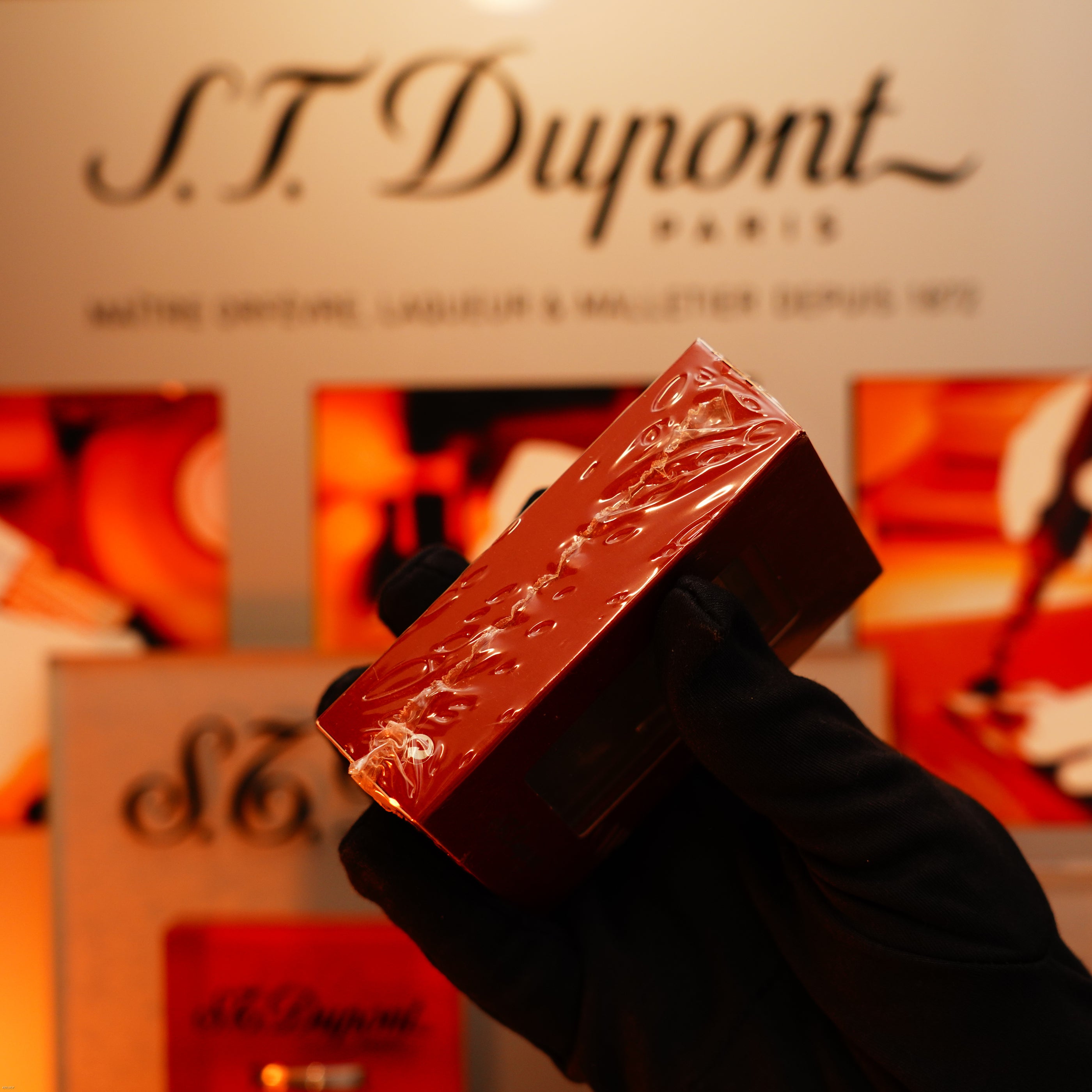 A gloved hand holds a sealed Vintage 1990 St Dupont Heavy Silver Vertical Ligne Lighter from Lucy Lighter, displayed before a branded backdrop to emphasize the product’s rarity and quality.