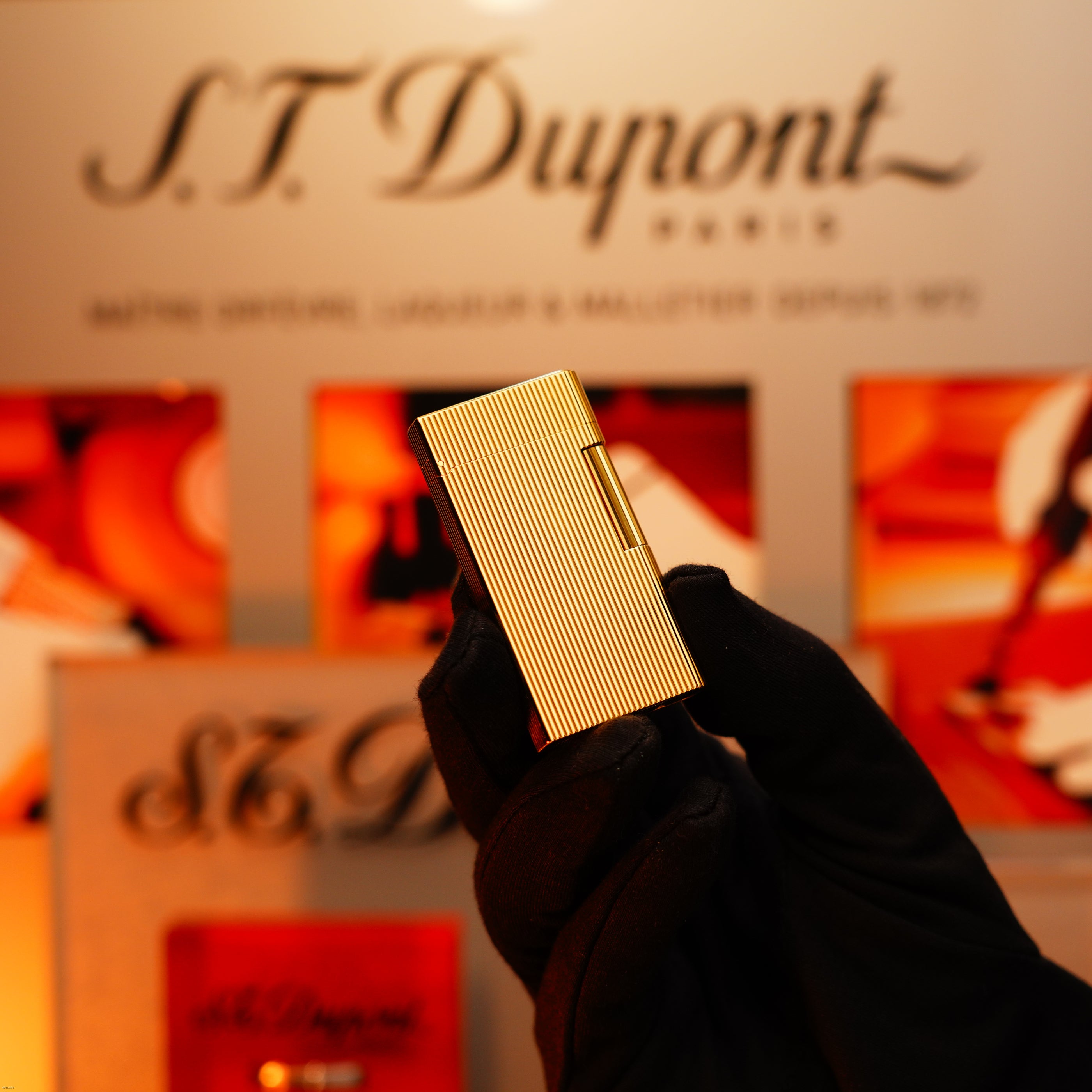 A gloved hand holds a Vintage 1970 Heavy 24k Gold Finish Caran d'Ache Limited Madison Lighter by Lucy Lighter before a blurred display, showcasing this extremely rare Swiss luxury piece with a 12-month functional warranty.