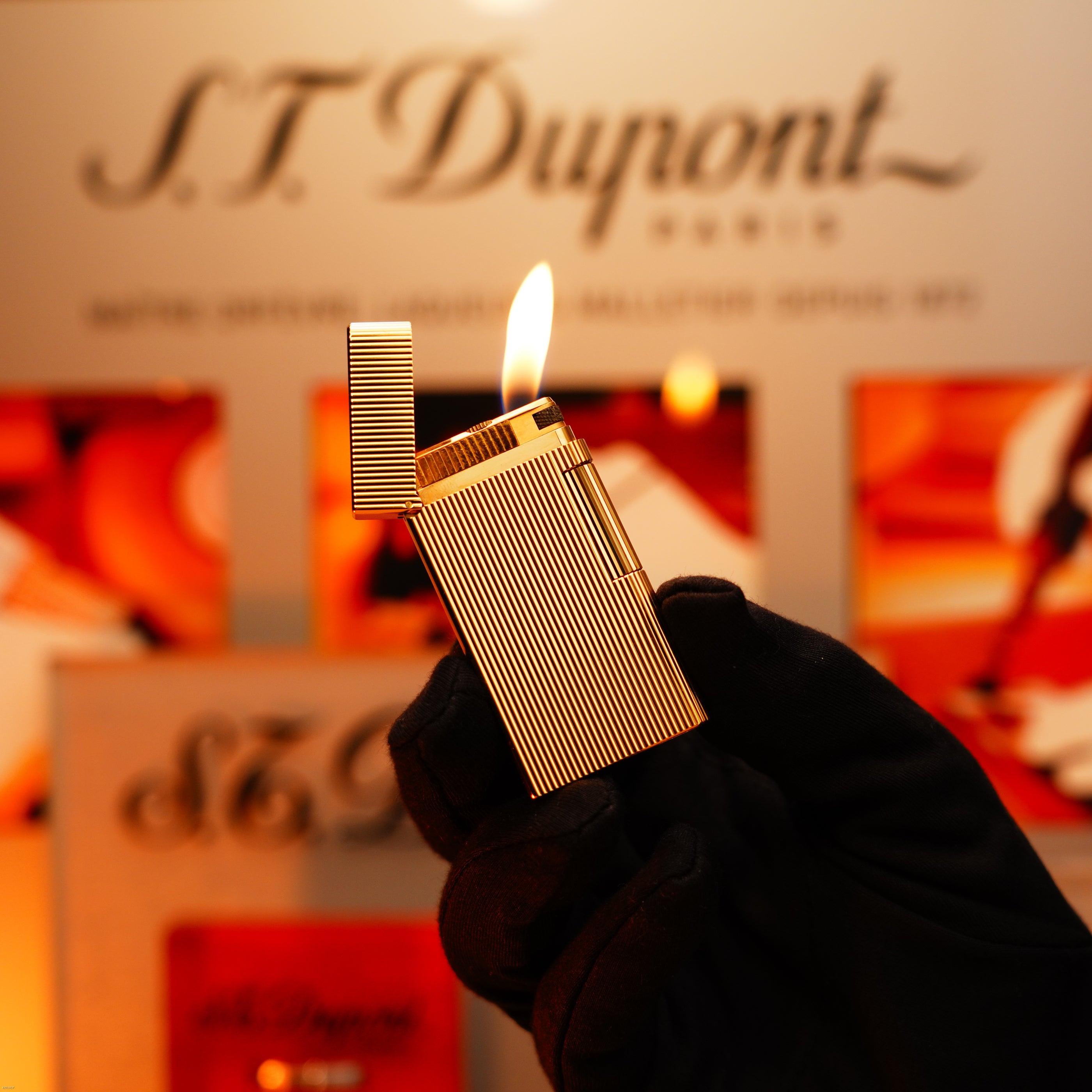 A gloved hand holds a Vintage 1970 Heavy 24k Gold Finish Caran d'Ache Limited Madison Swiss Lighter by Lucy Lighter, open with a lit flame, against a blurred backdrop; covered by a 12-month warranty for functional issues.