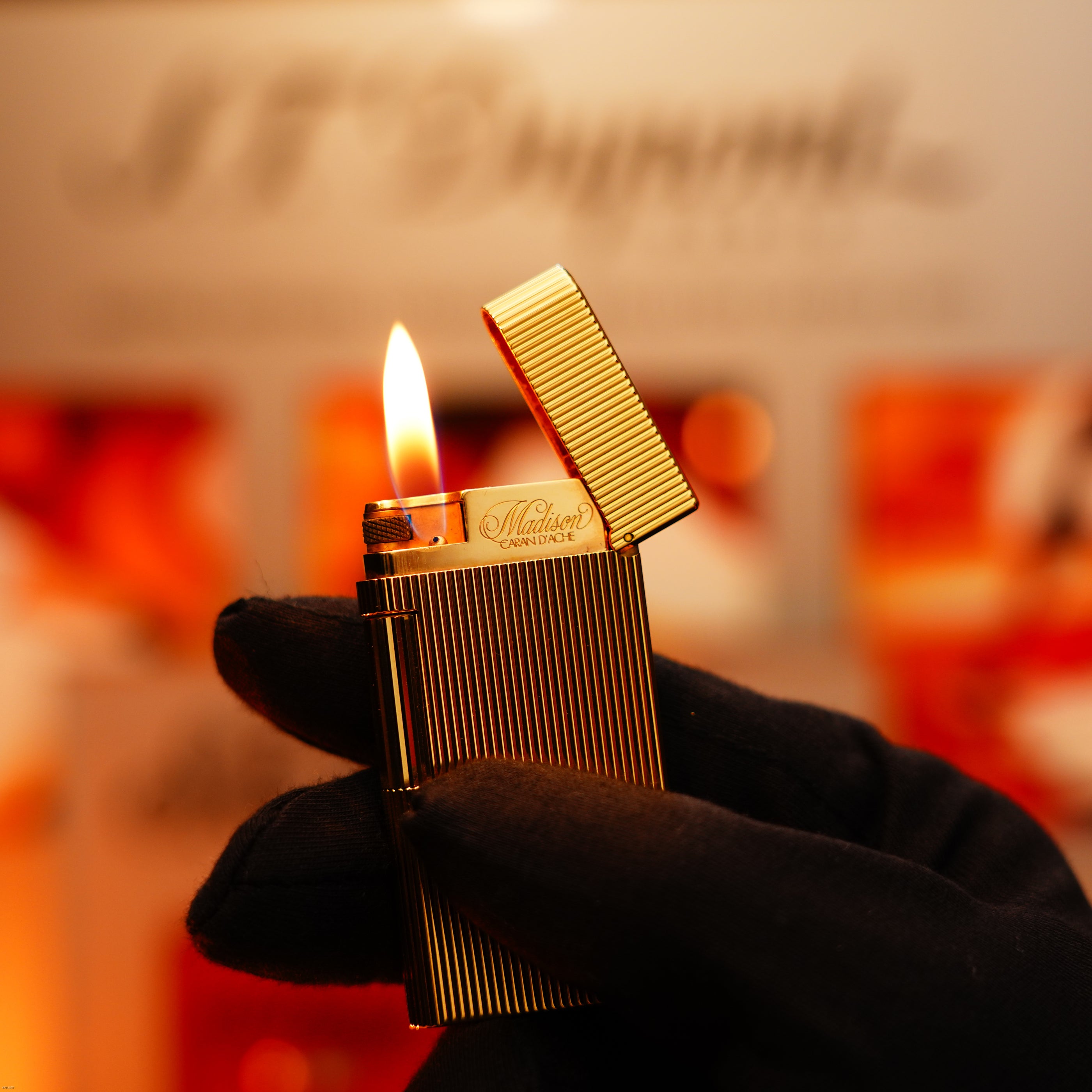 A gloved hand holds a Vintage 1970 Heavy 24k Gold Finish Caran d'Ache Limited Madison Swiss Lighter by Lucy Lighter, lid open with a visible flame, backed by a 12-month warranty against functional issues.