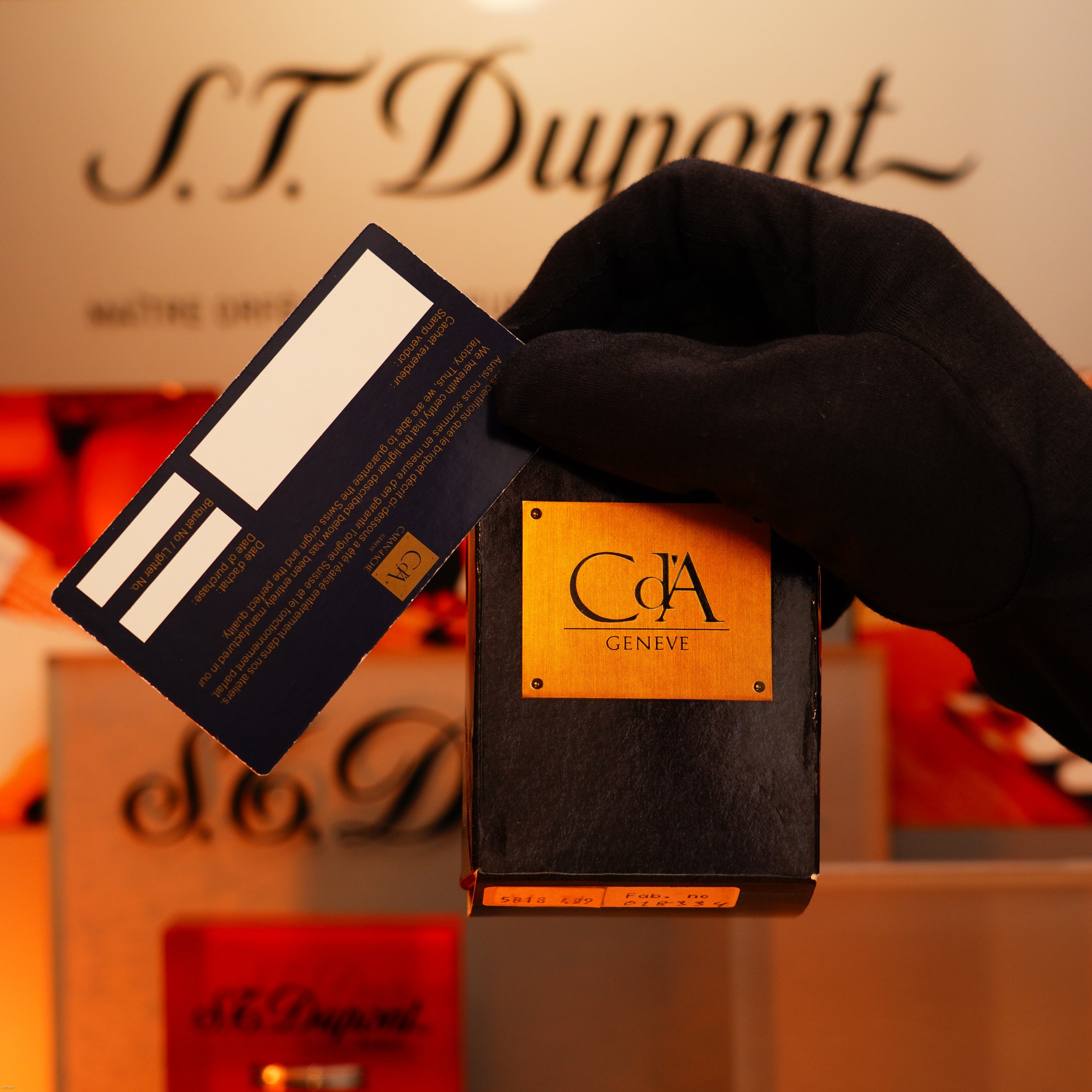 A gloved hand holds a black and gold Lucy Lighter box and card—possibly for the Vintage 1970 Heavy 24k Gold Finish Caran d'Ache Limited Madison Swiss Lighter—with a 12-month warranty for functional issues.