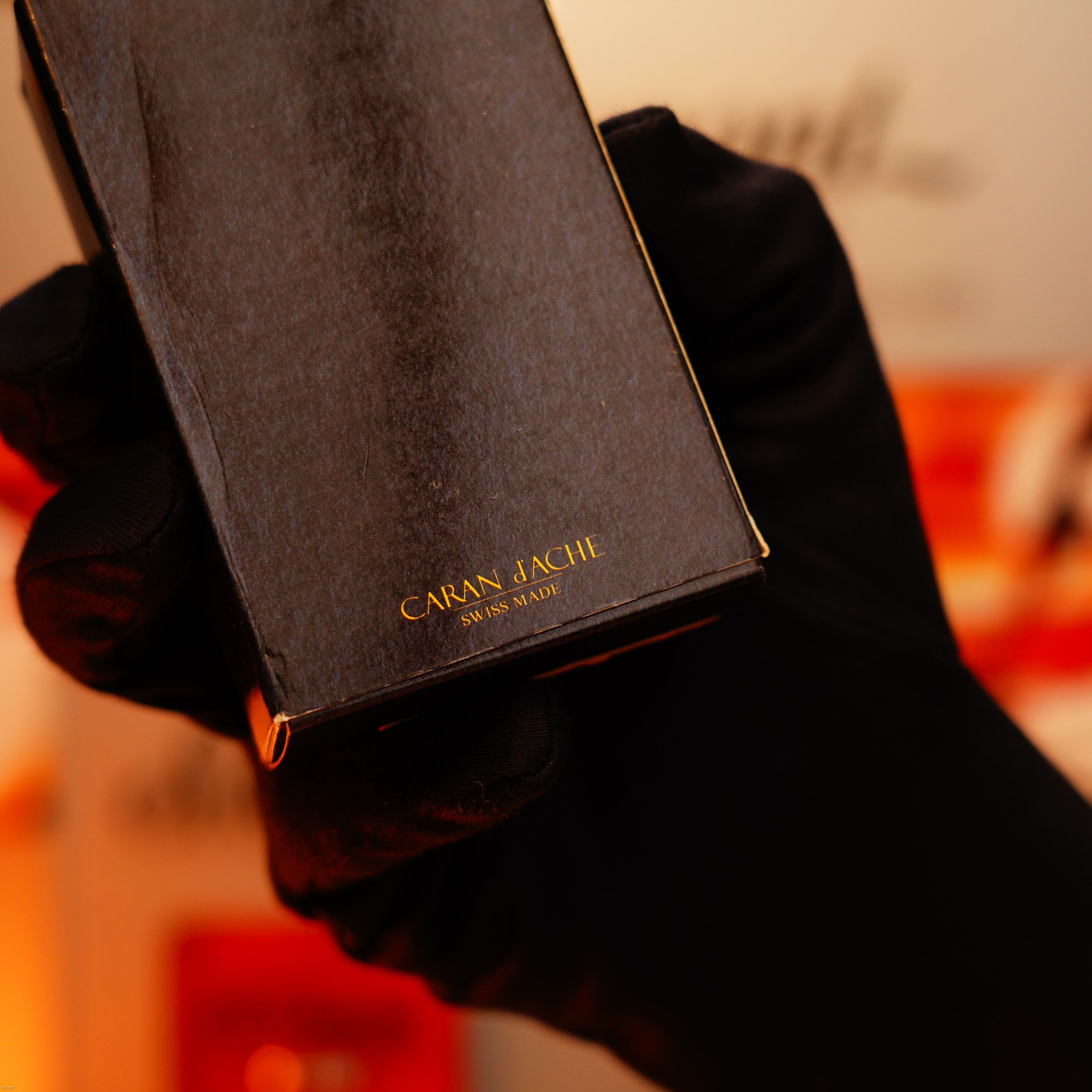 A gloved hand holds a Lucy Lighter Vintage 1970 Heavy 24k Gold Finish Caran d’Ache Madison—an extremely rare, limited-edition Swiss lighter—against a blurred background.