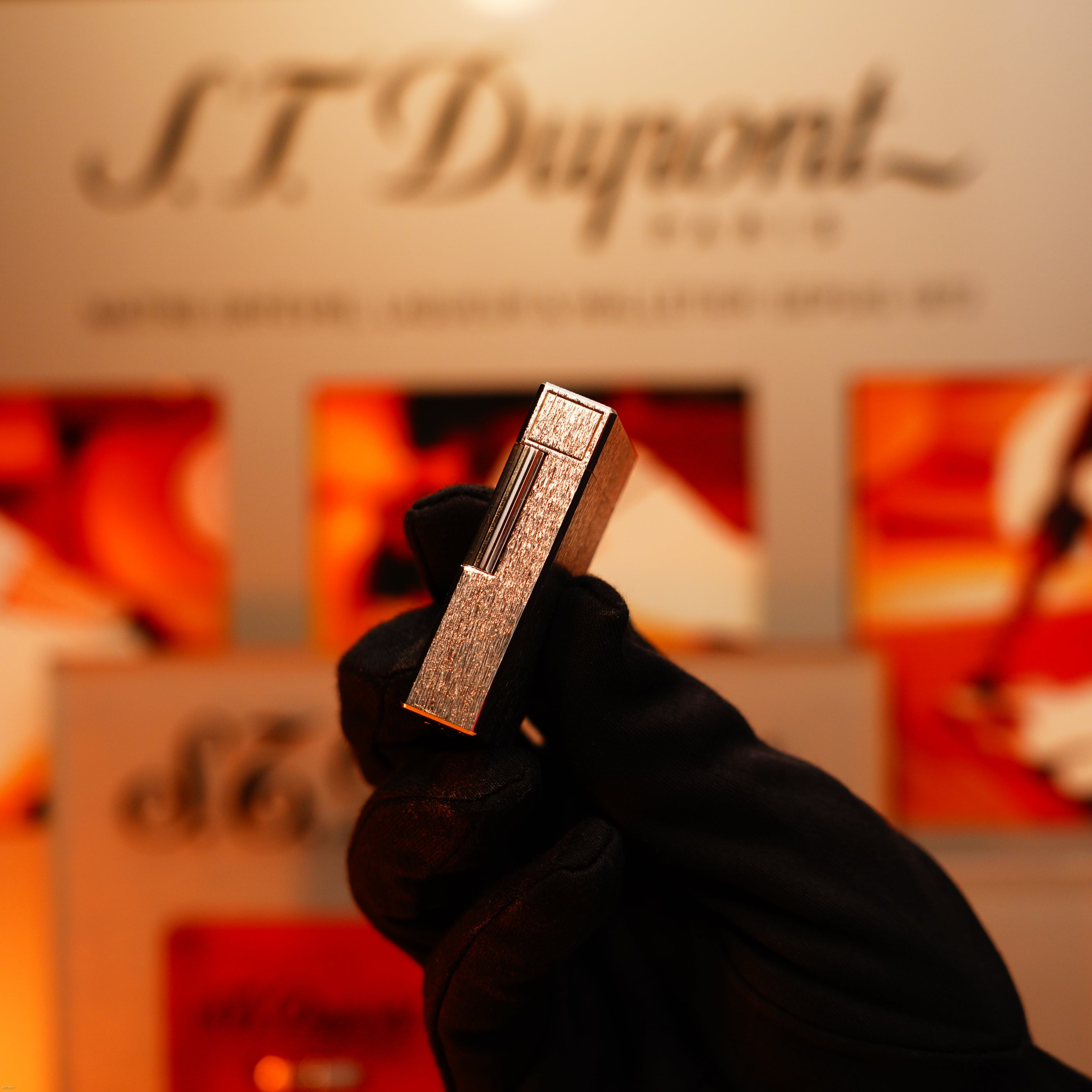 A gloved hand holds a Vintage 1980 Lucy Lighter Heavy Silver Finish Ligne 1 Large Rare Pattern Lighter in front of a blurred display, highlighting its timeless elegance and lasting quality.