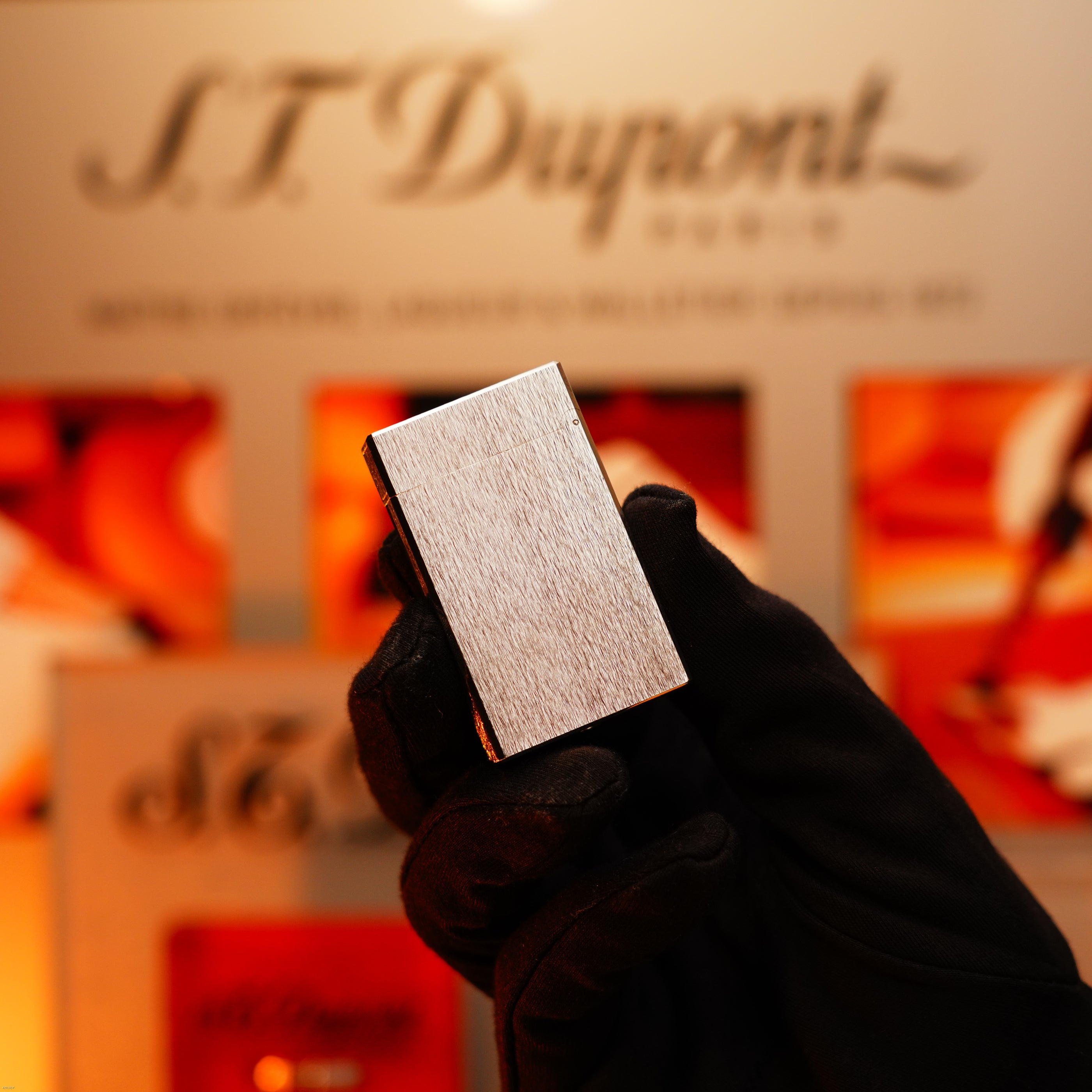 A gloved hand holds the Lucy Lighter Vintage 1980 St Dupont Ligne 1 Large, a rare heavy silver finish luxury lighter, with its brushed metal reflecting timeless style and quality in front of a blurred display.