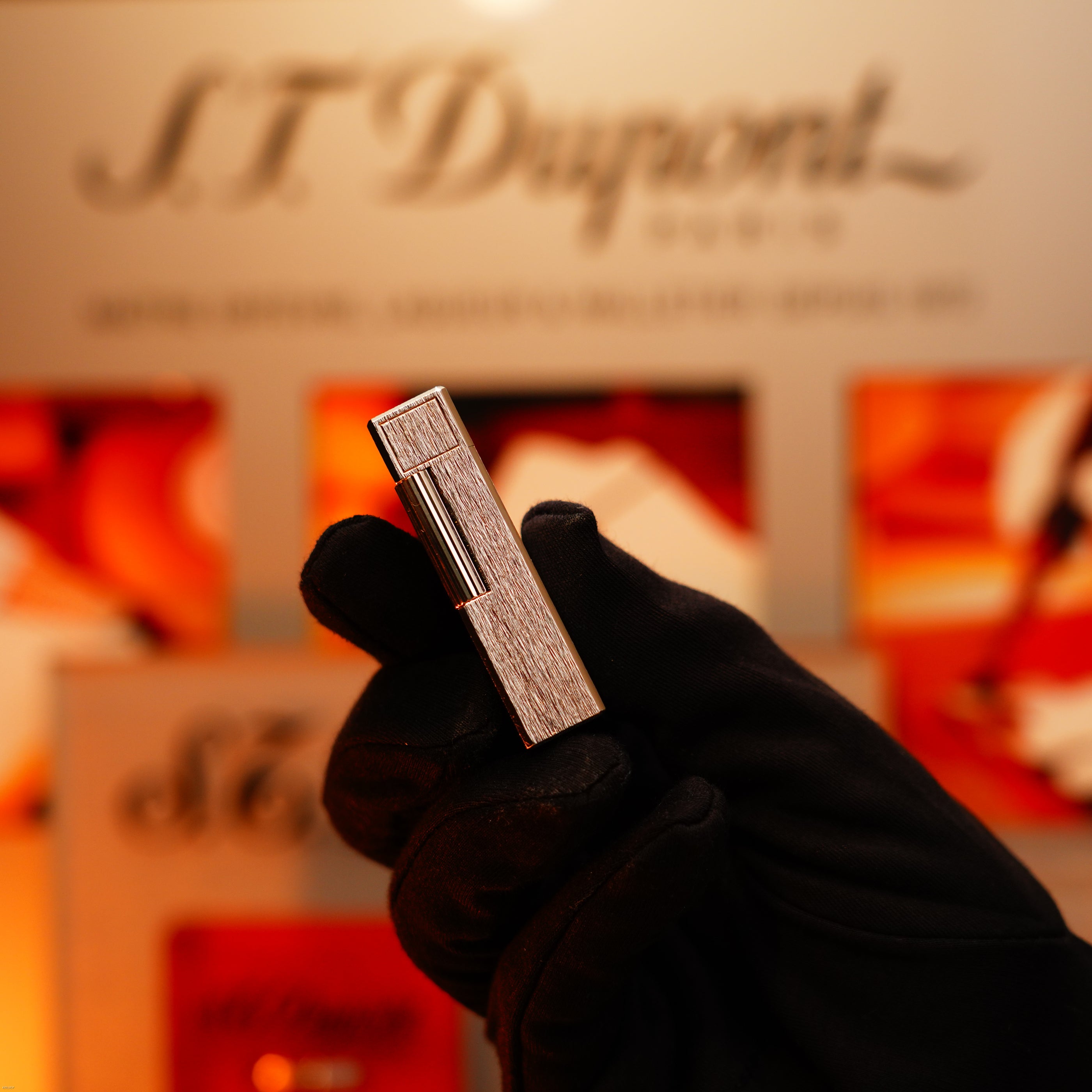 A gloved hand holds a Vintage 1980 Heavy Silver Finish Ligne 1 Large size Rare Pattern Lighter by Lucy Lighter against a blurred background with the brand logo and packaging, symbolizing enduring elegance and quality.