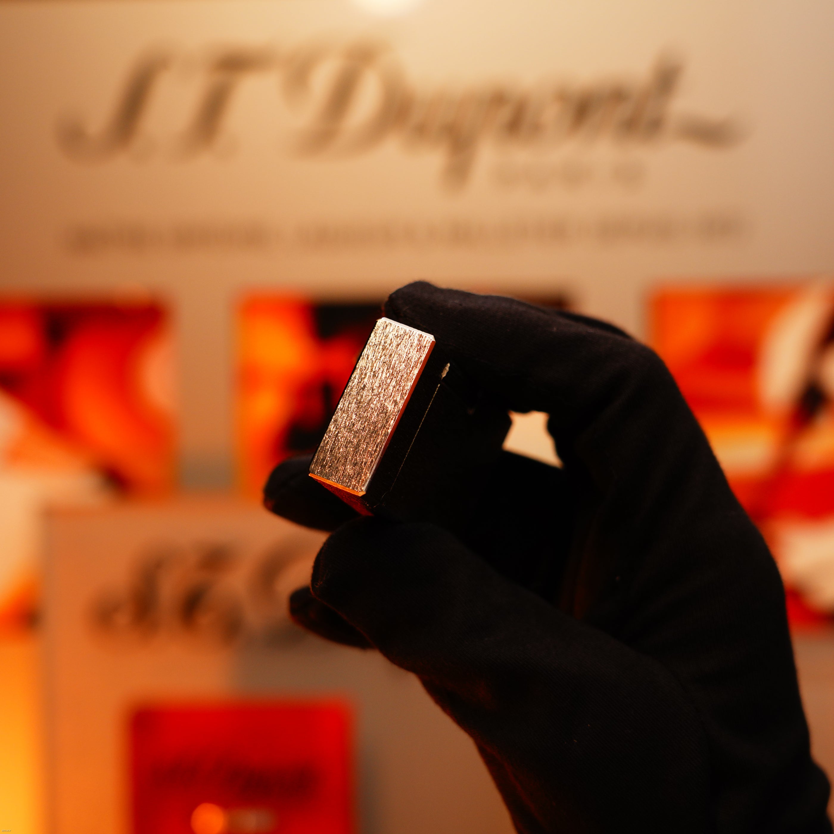 A gloved hand holds a Vintage 1980 St Dupont Heavy Silver Finish Ligne 1 Large size Rare Pattern Lighter by Lucy Lighter, with a blurred display in the background.