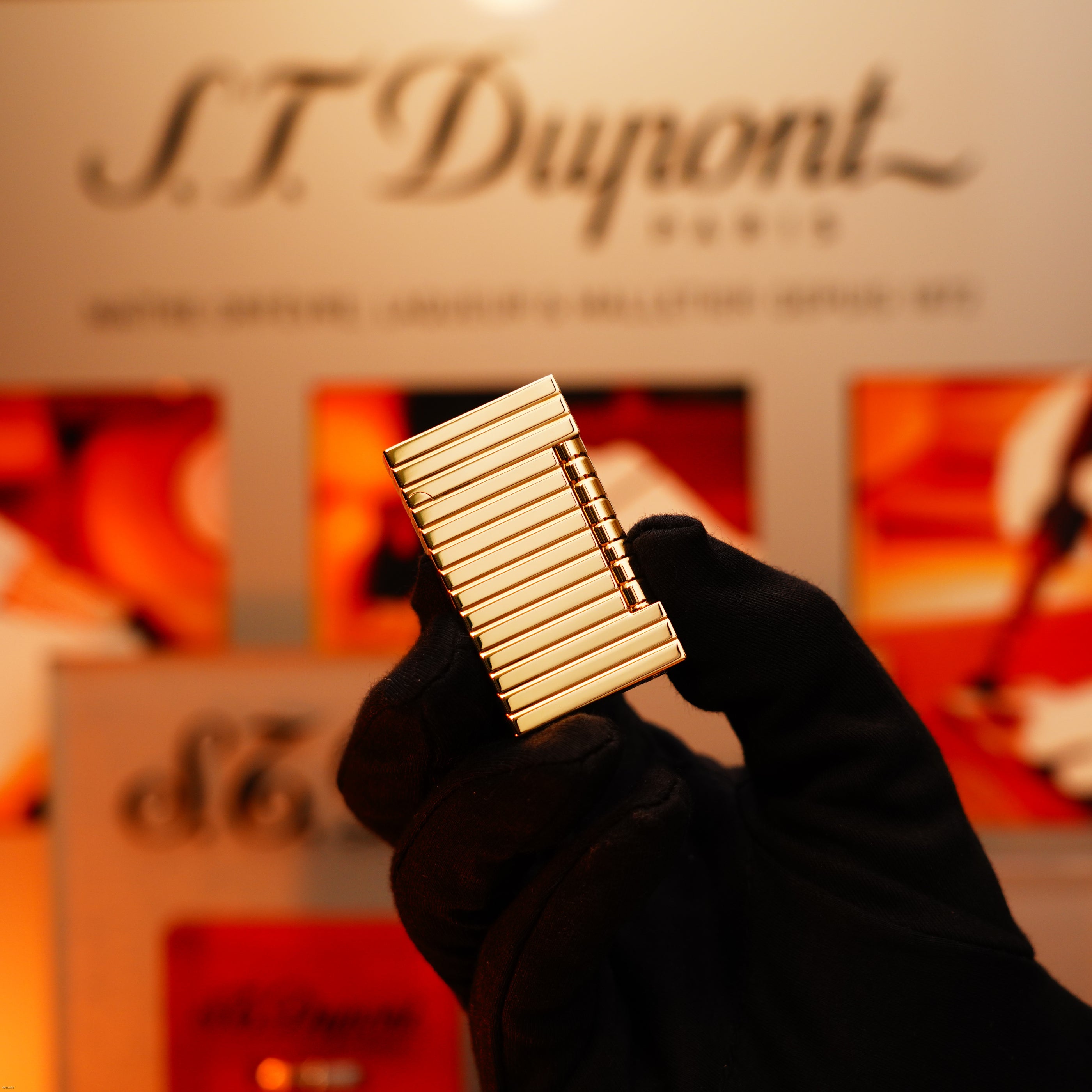 A gloved hand holds a Vintage 1970 Ultra Rare 1/1 Solid 18K Gold Masterpiece lighter by Lucy Lighter in front of a blurred branded background.