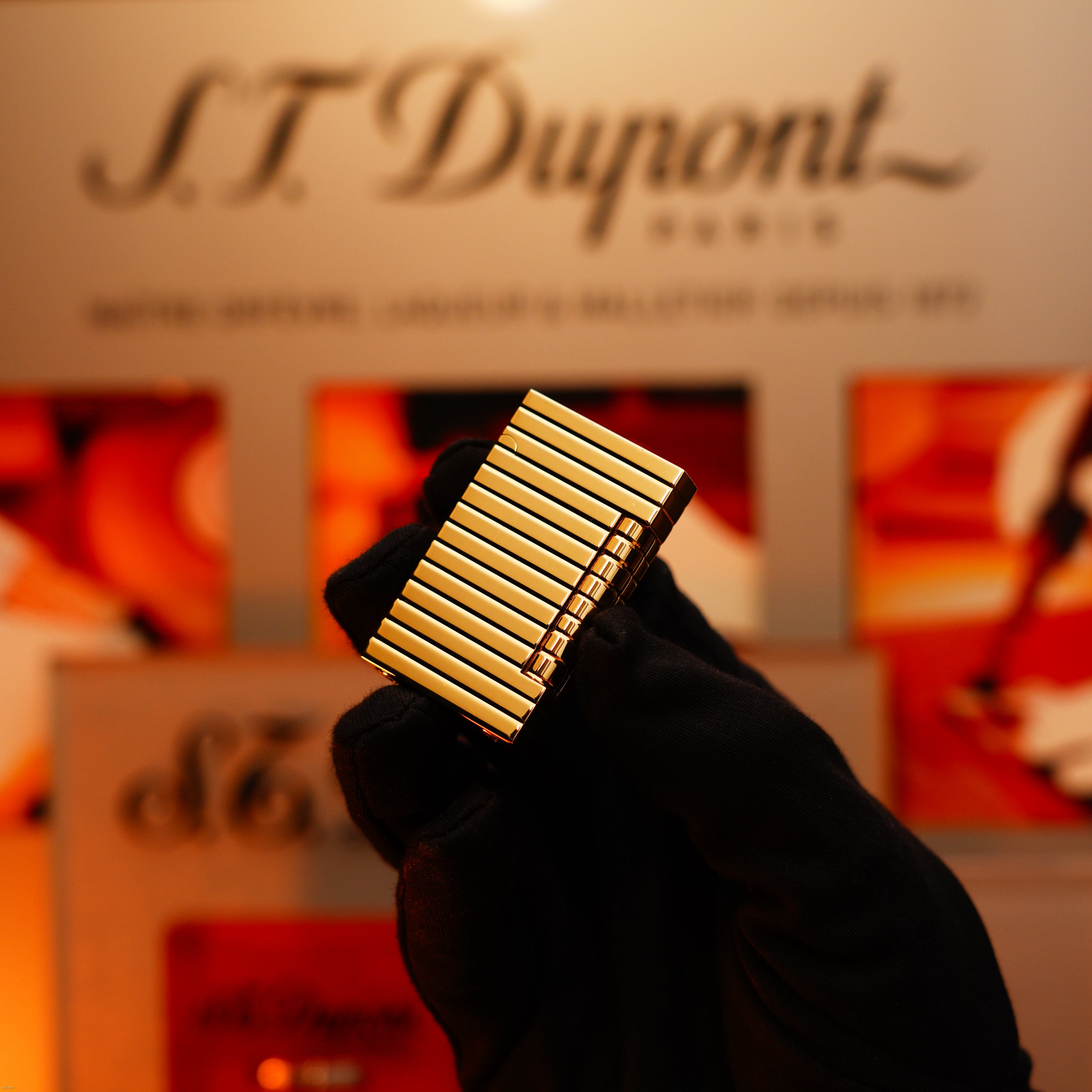 A gloved hand holds the ultra rare Vintage 1970 ST Dupont Lighter—Solid 18K Gold Masterpiece by Lucy Lighter, displayed before a blurred branded backdrop, capturing luxury and exclusivity.
