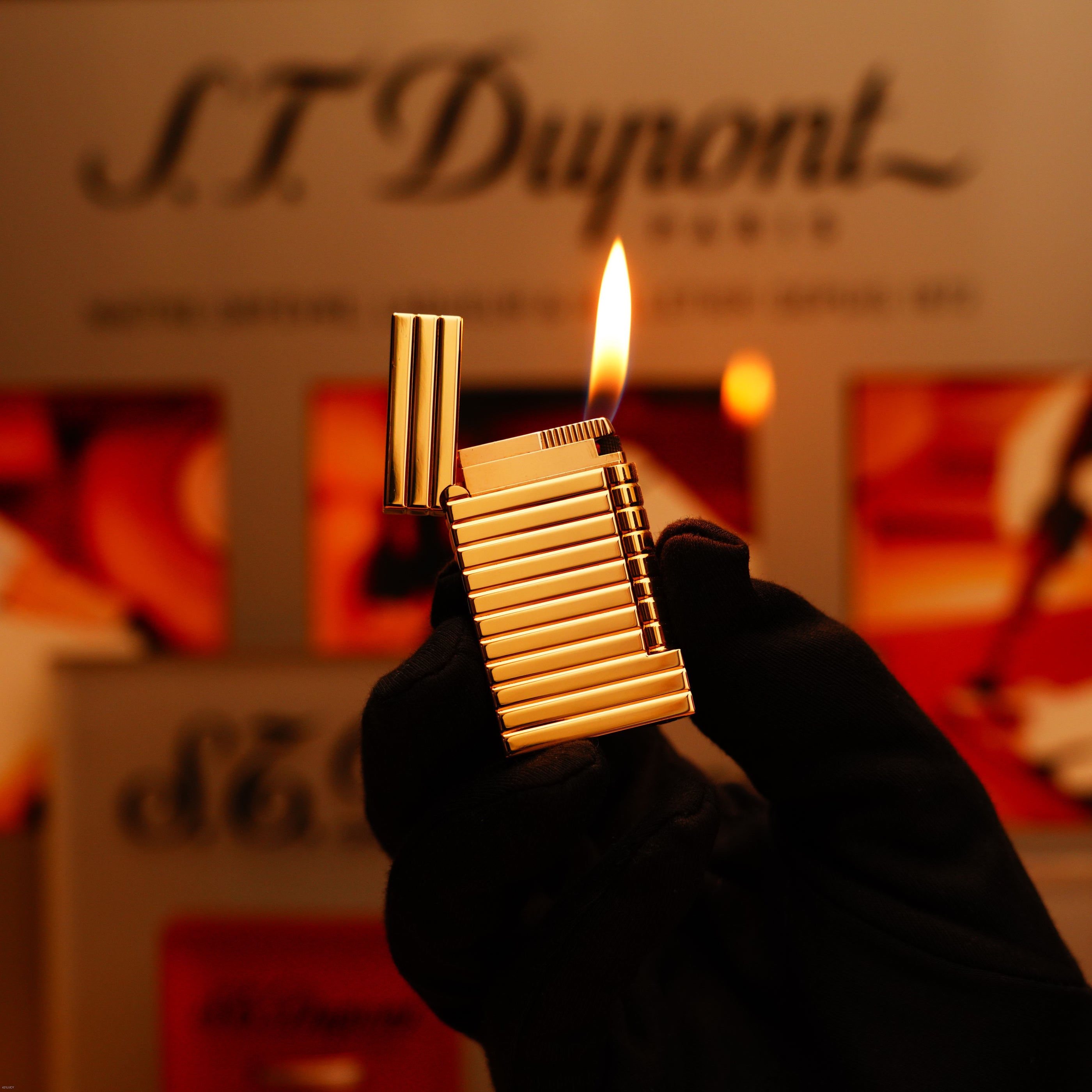 A gloved hand holds the ultra-rare Vintage 1970 ST Dupont Lighter – Solid 18K Gold Masterpiece by Lucy Lighter against a blurred background with the brand’s logo, emphasizing its timeless elegance and exclusivity.
