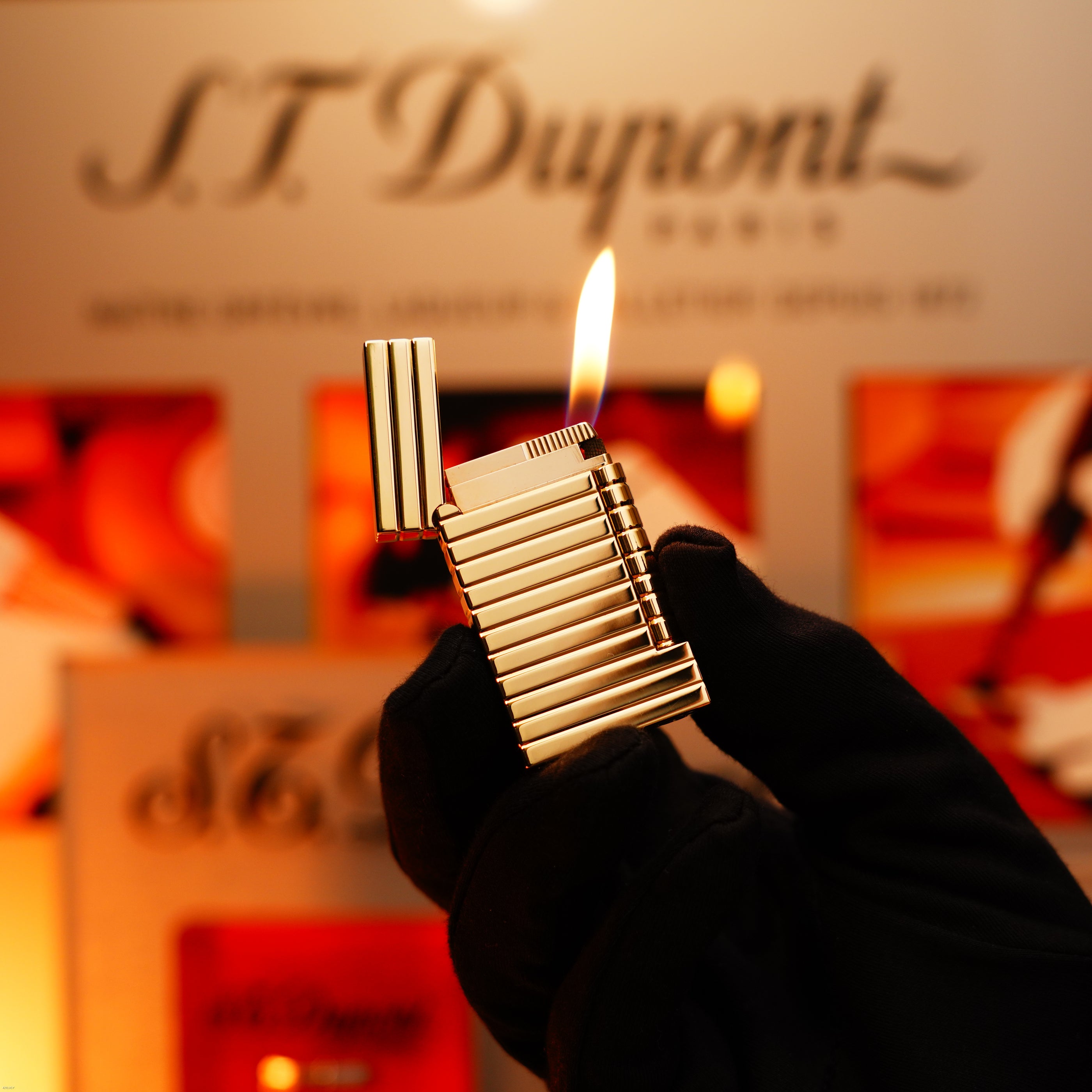 A gloved hand holds an open, lit Vintage 1970 Ultra Rare 1/1 ST Dupont Lighter—Solid 18K Gold Masterpiece by Lucy Lighter before a blurred display with the brand’s logo and products.
