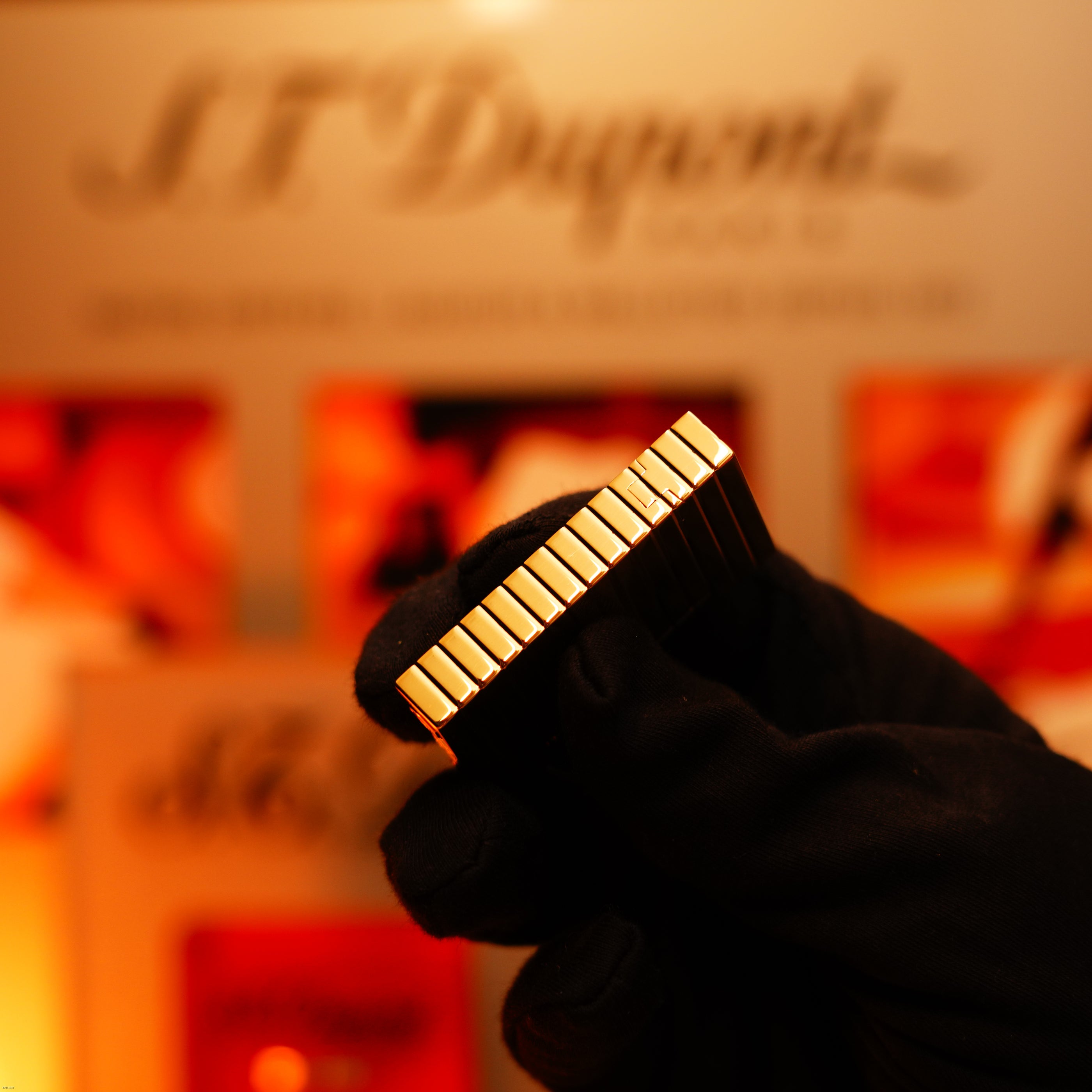 A gloved hand holds the Lucy Lighter Vintage 1970 Ultra Rare Solid 18K Gold S.T. Dupont Lighter masterpiece, set against a blurred background with the S.T. Dupont logo.